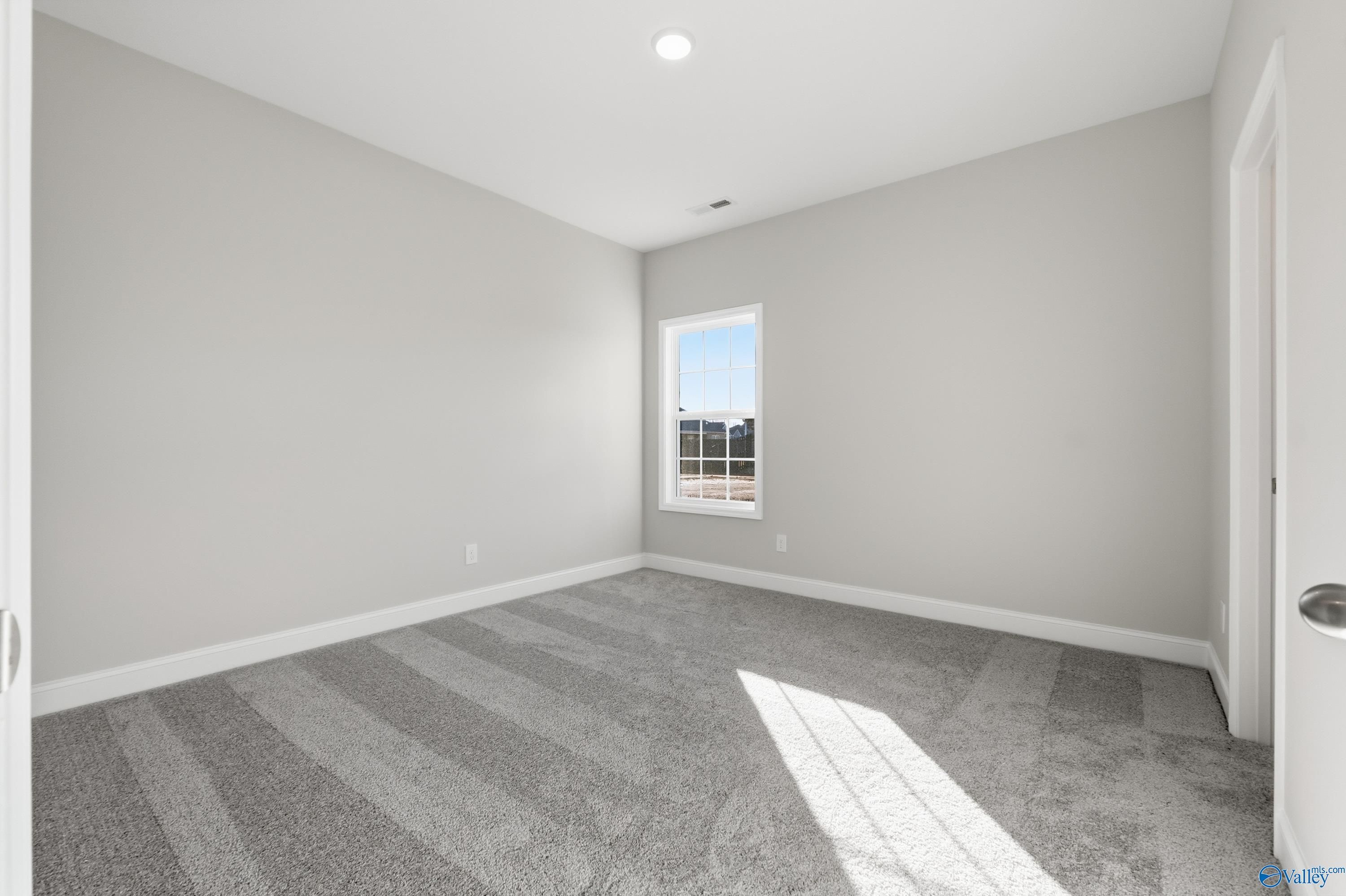 Sunlit empty bedroom with neutral gray walls, plush carpet, and large window in Davidson Homes Montgomery B, Toney, AL