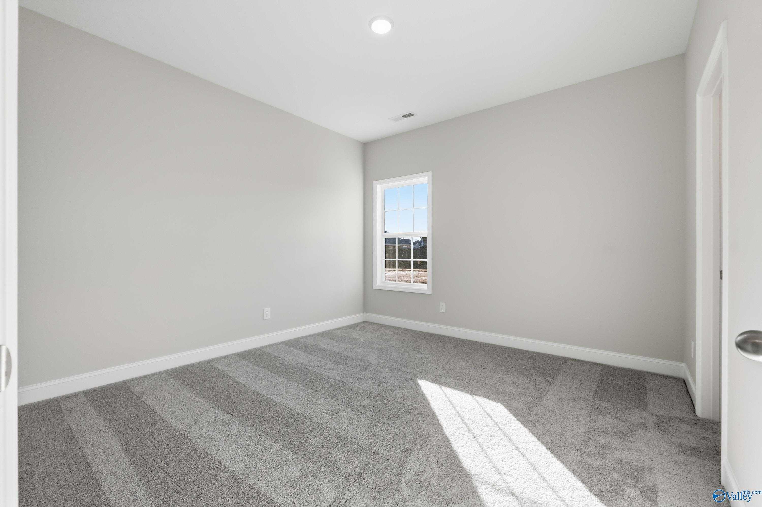 Sunlit empty bedroom with neutral gray walls, plush carpet, and large window in Davidson Homes Montgomery B, Toney, AL