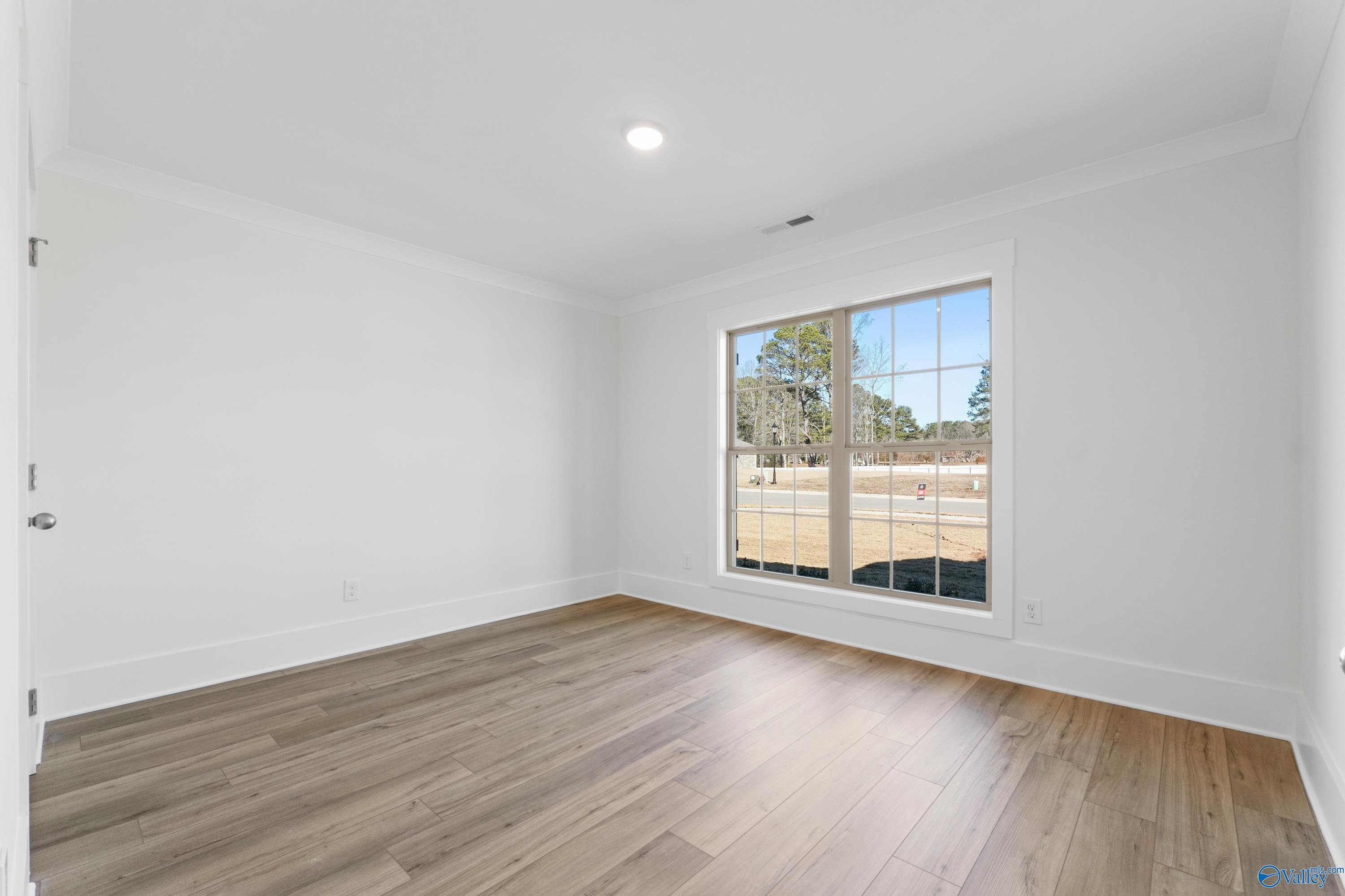 Bright empty bedroom with large window overlooking yard and hardwood floors in The Daphne C, Davidson Homes, Arab, Alabama