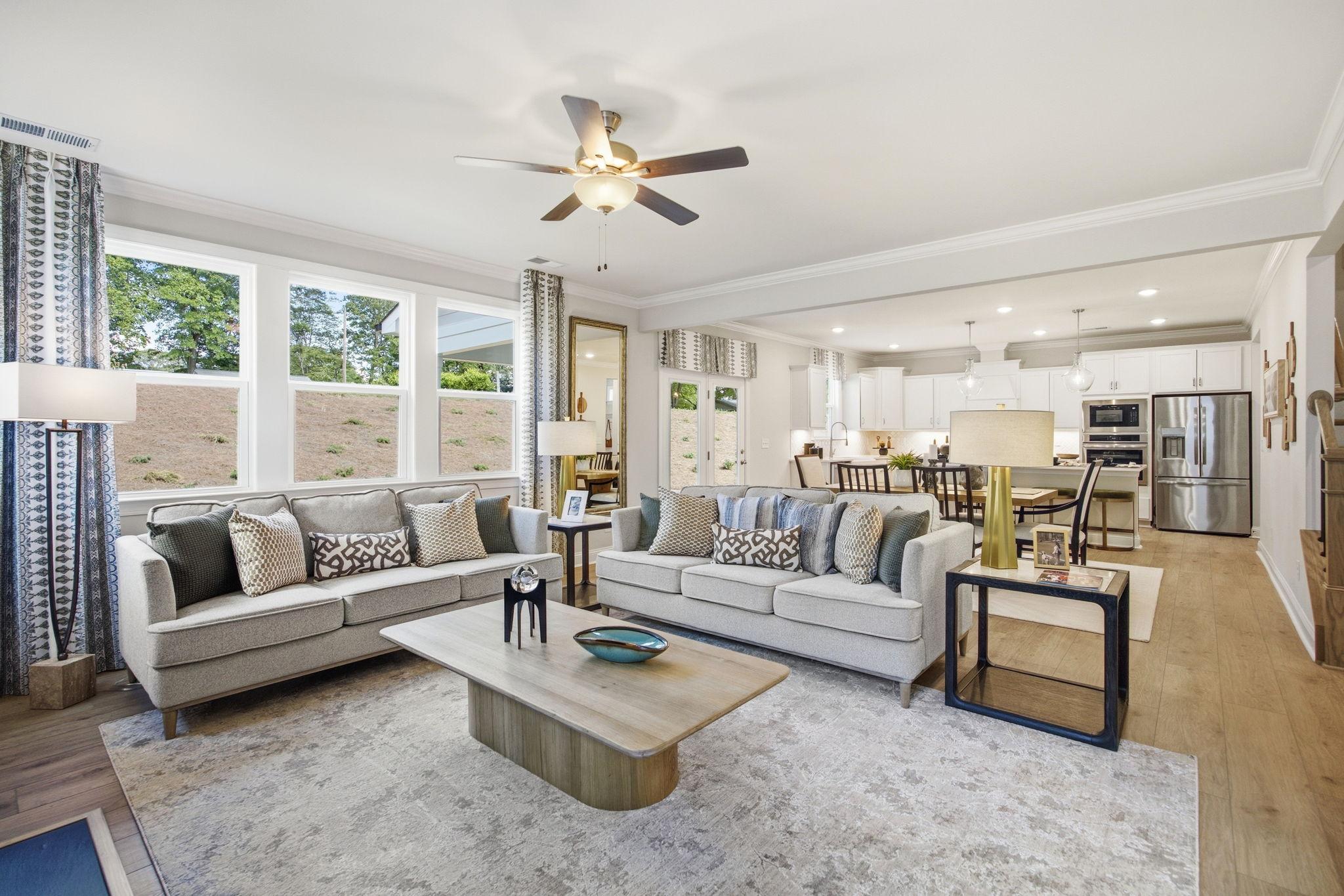 Open-concept living room at Enclave at Belmont in Belmont NC with gray sofas, hardwood floors, ceiling fan, and open kitchen