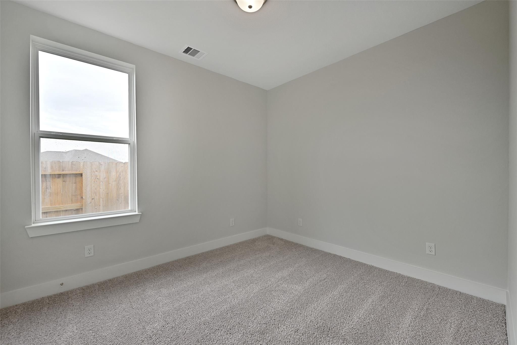 Bright secondary bedroom with gray walls, carpet floor, and large window in Davidson Homes The Edward A, Lago Mar, Texas City