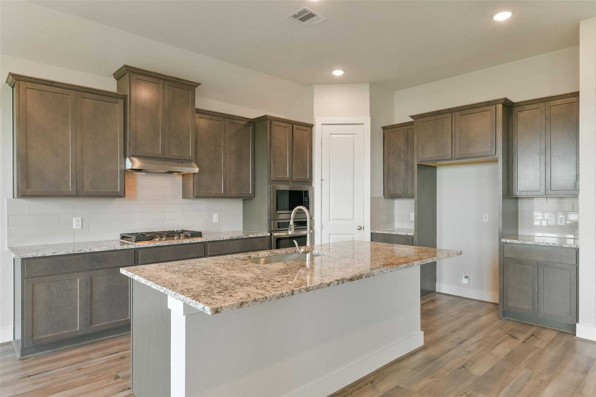 Modern kitchen with granite island, shaker cabinets, and stainless appliances in Davidson Homes The Edward A, Lago Mar, Texas