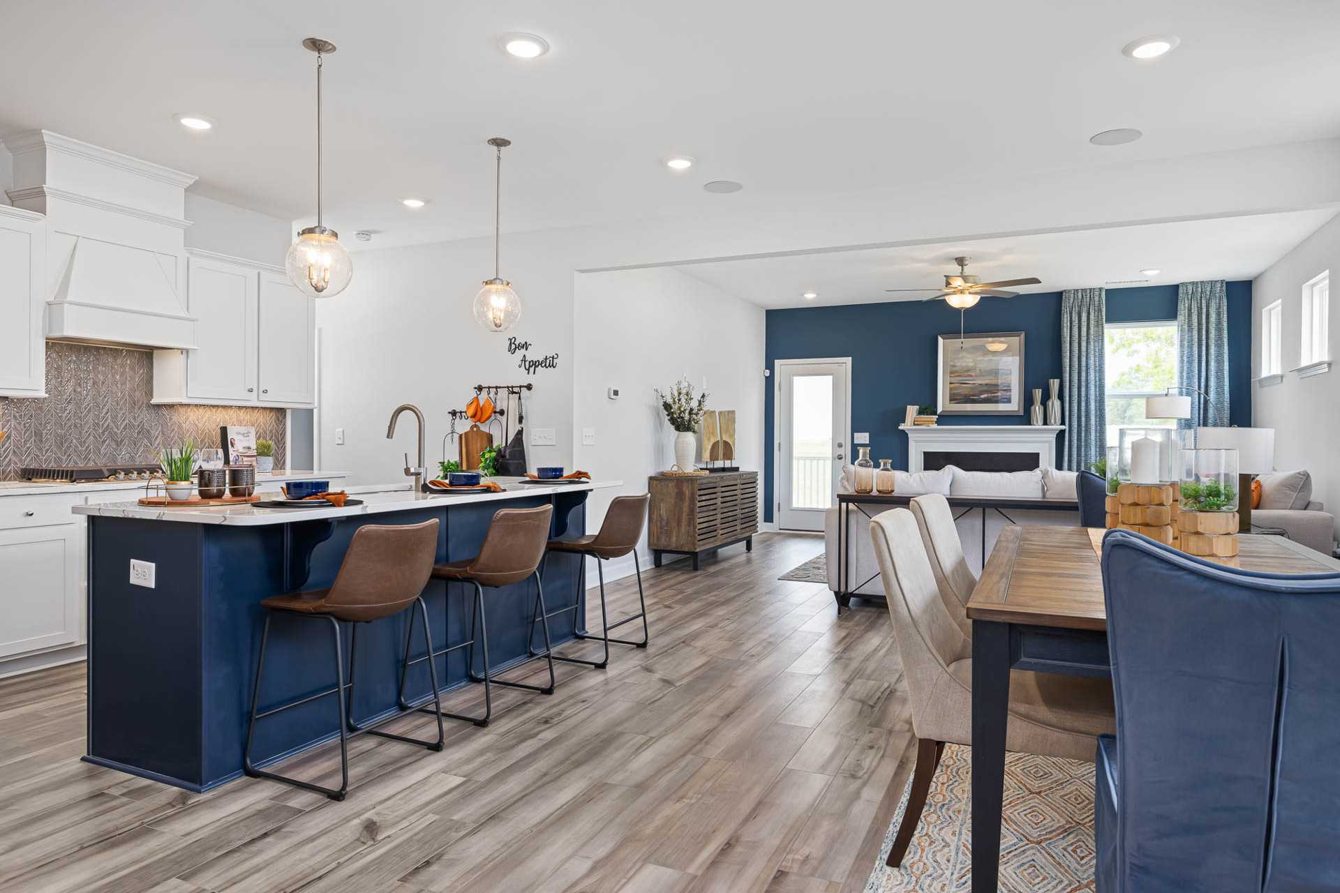 Open-concept kitchen dining area in Beverly Place Four Oaks NC with navy island bar stools hardwood floors and modern accents
