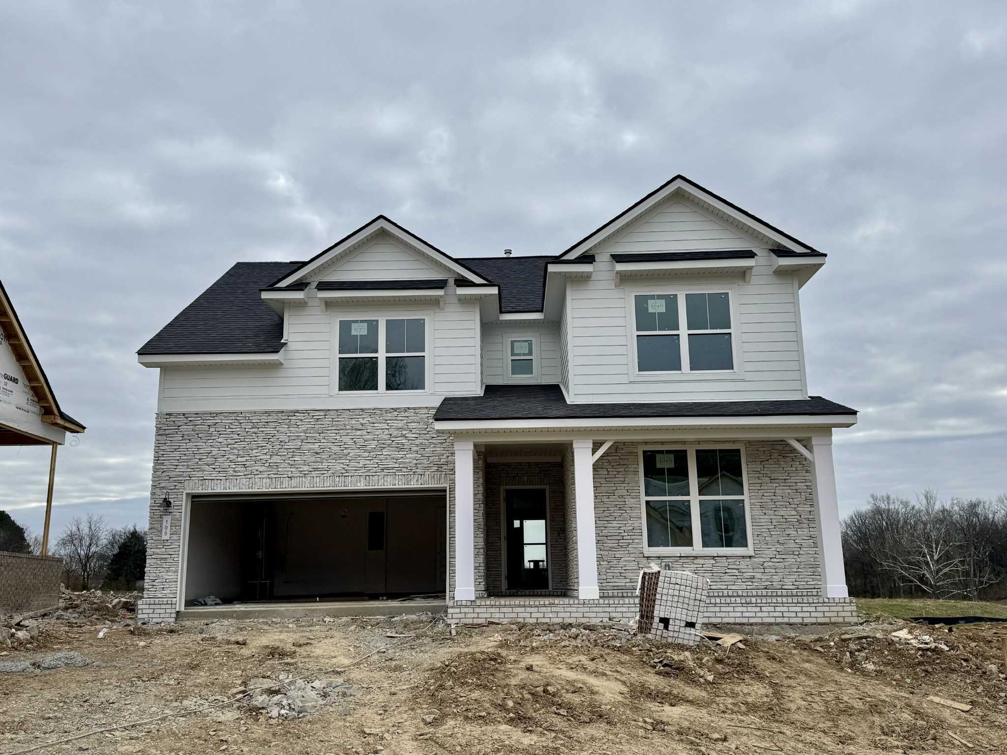 Two-story Ridgeport home exterior with white brick siding, black gable roof, open 2-car garage, and columned front porch in Woods Crossing, Gallatin, Tennessee