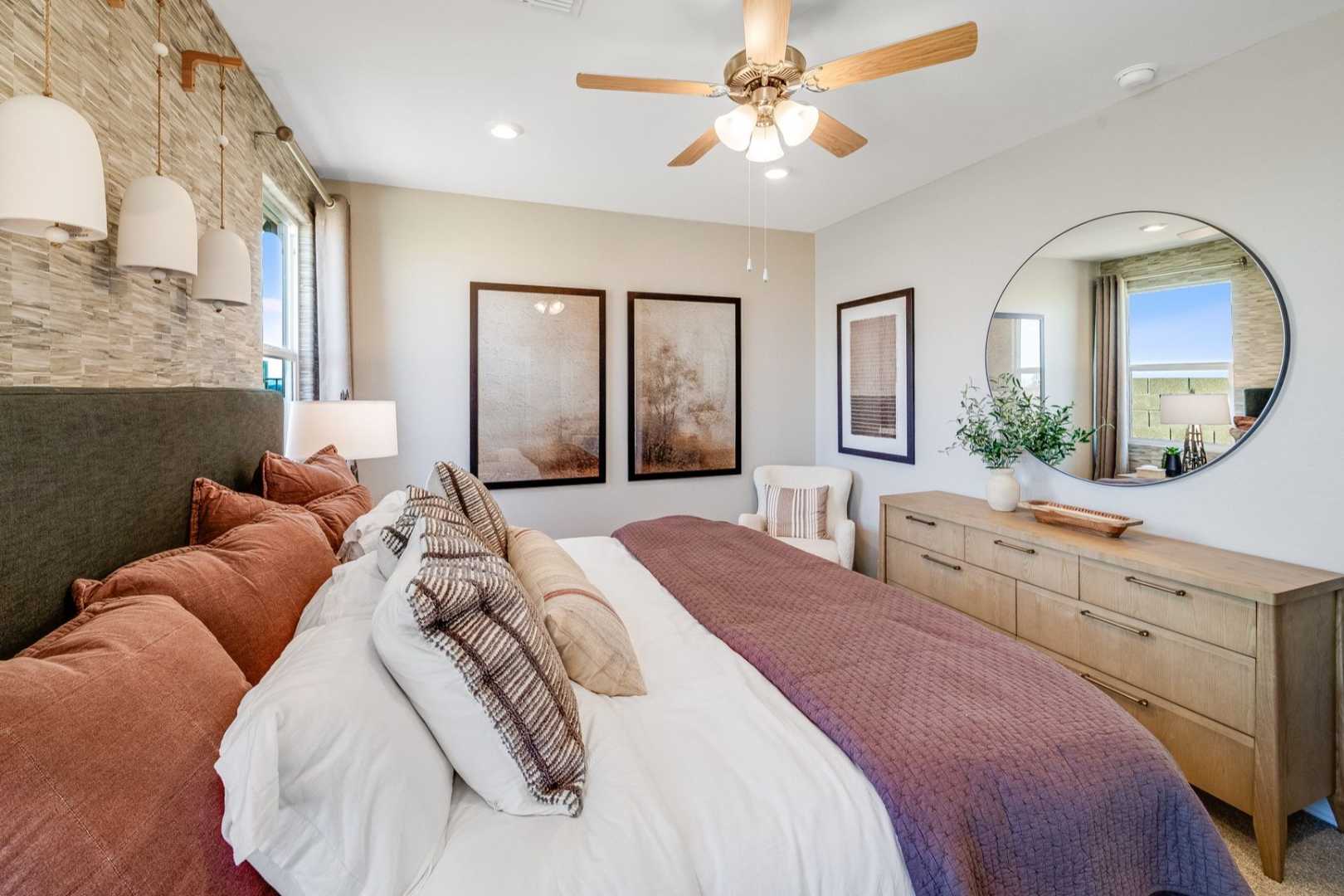 Spacious master bedroom in The Savannah C featuring king bed with plush pillows, round mirror over oak dresser, ceiling fan, and neutral accents