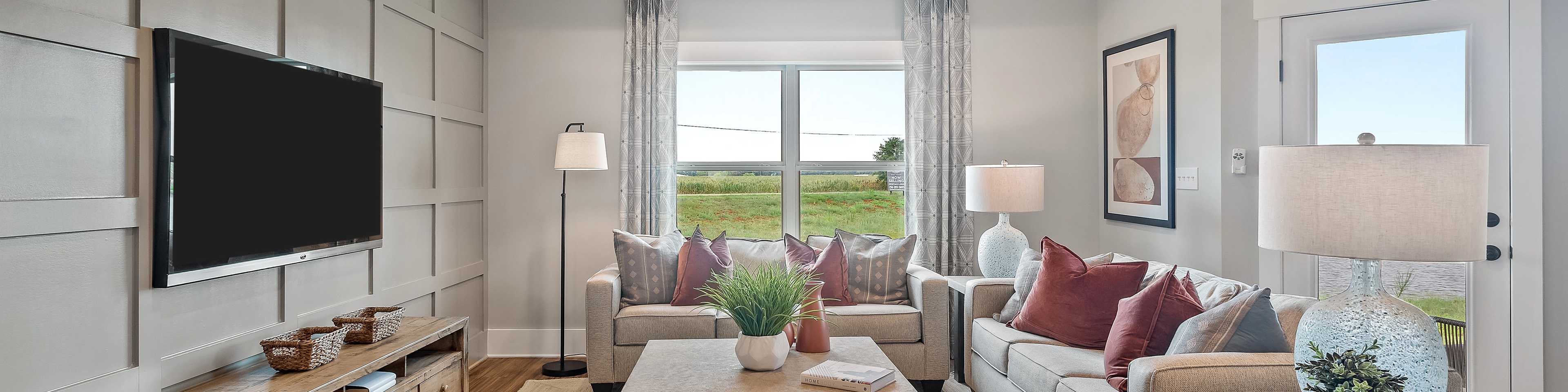 Spacious living room in Heritage Lakes home, New Market Alabama with gray shiplap walls, mounted TV, plush L-shaped sofa, ceiling fan, and scenic window views