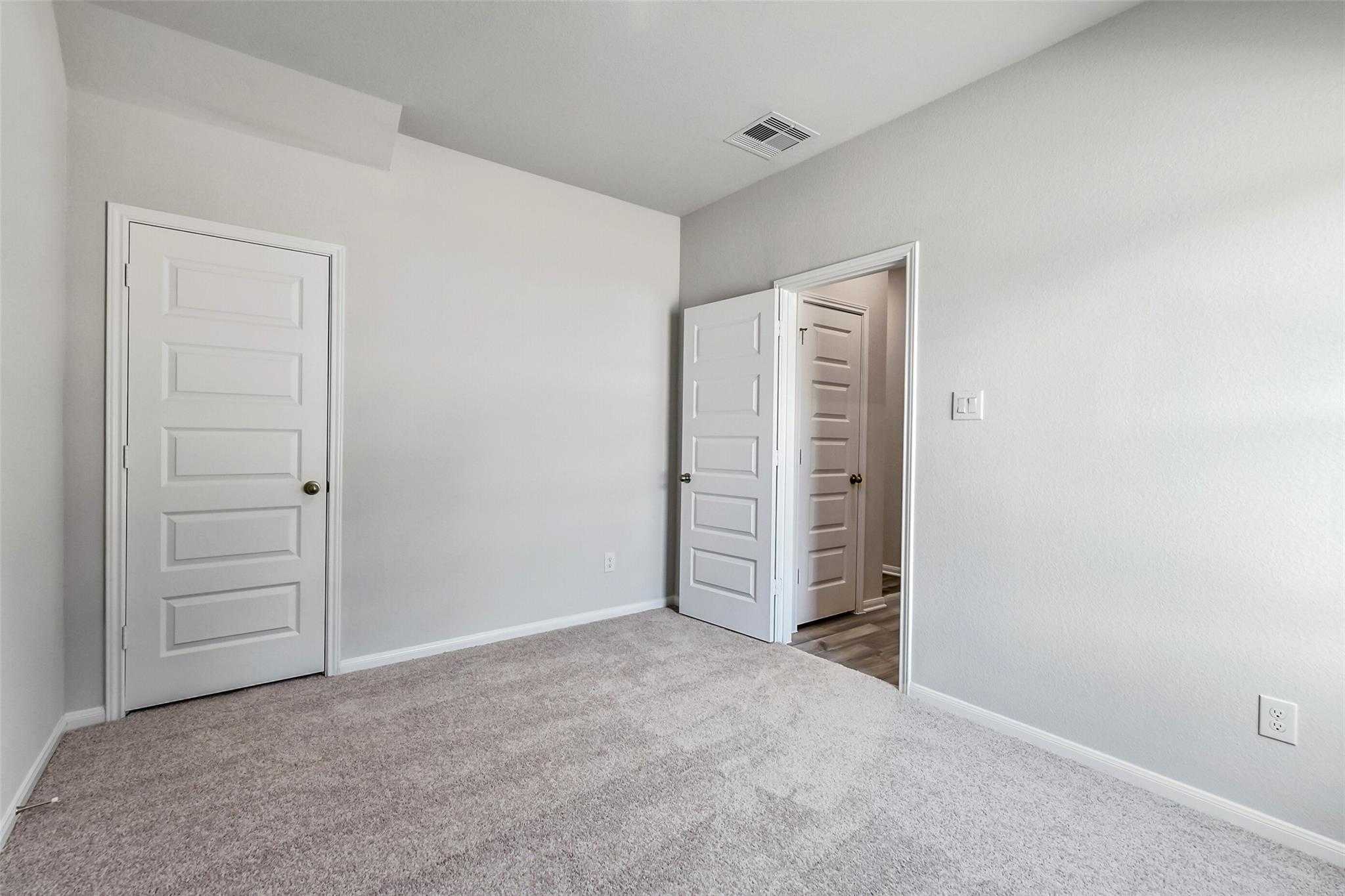 Spacious secondary bedroom with light gray walls, carpet floor, and double doors to bathroom in Davidson Homes The Sabine E, Conroe, Texas