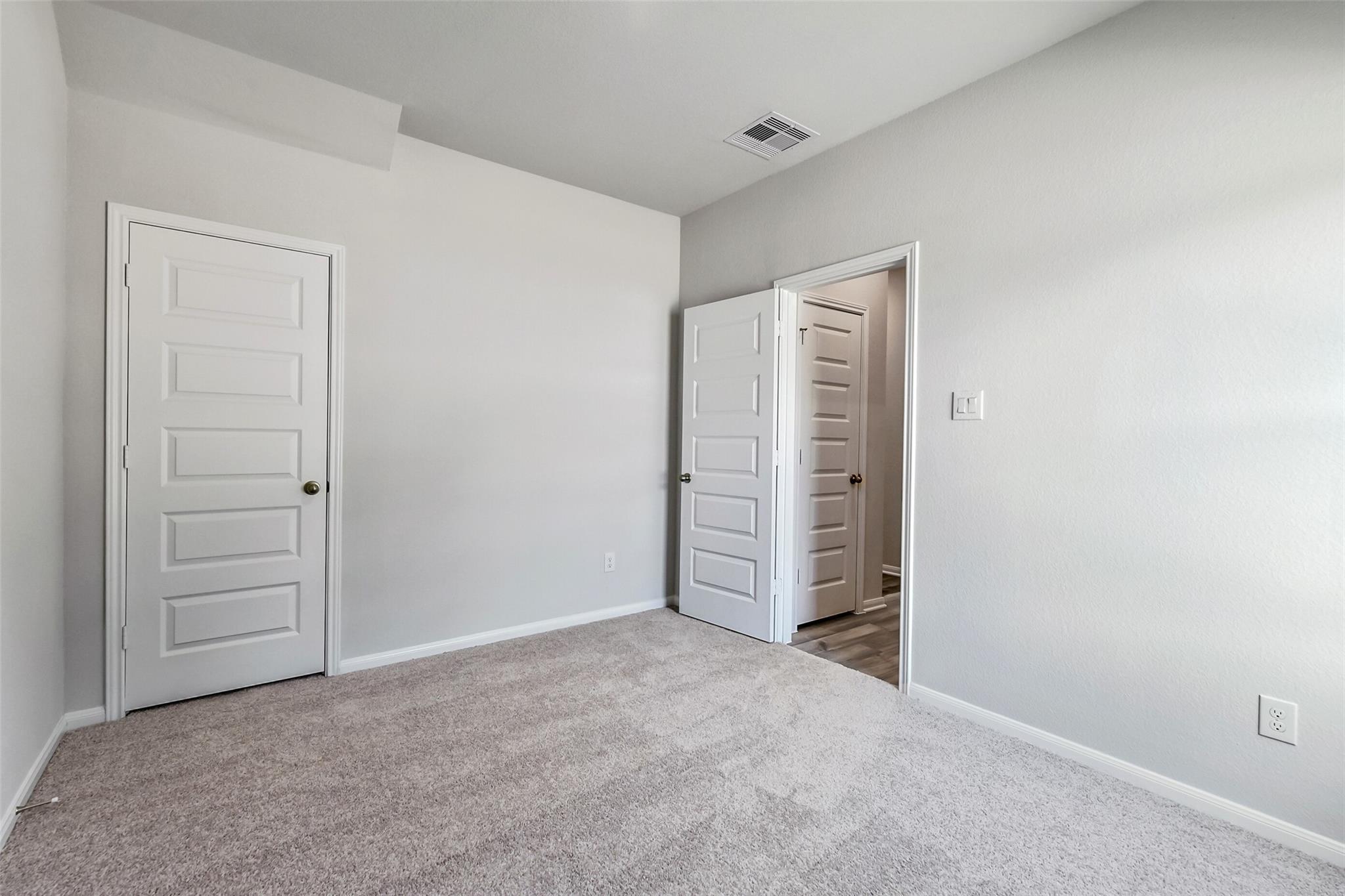 Spacious secondary bedroom with light gray walls, carpet floor, and double doors to bathroom in Davidson Homes The Sabine E, Conroe, Texas
