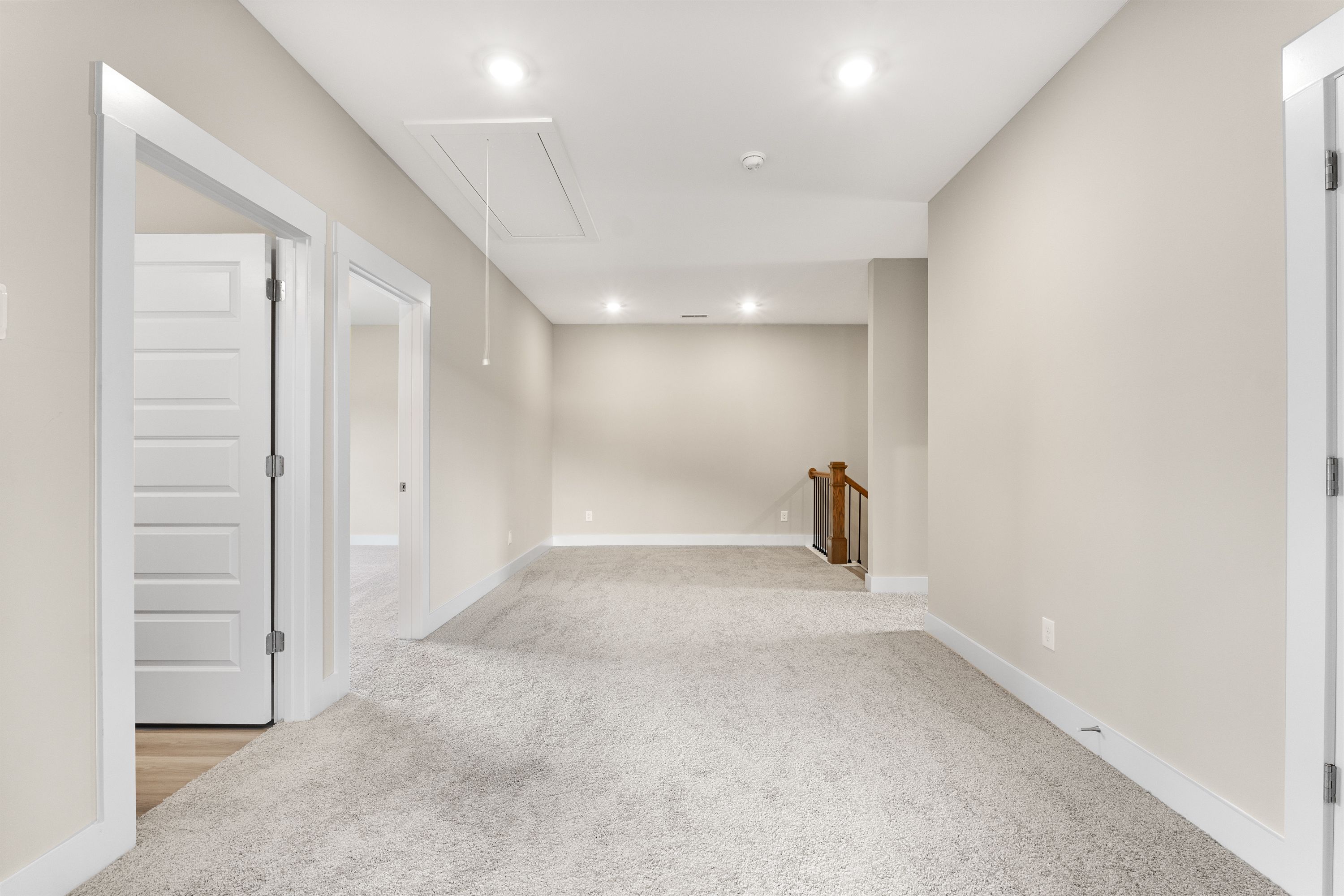 Spacious upstairs hallway in The Oxford A with beige walls, carpeted floors, open doorways, and wooden staircase railing