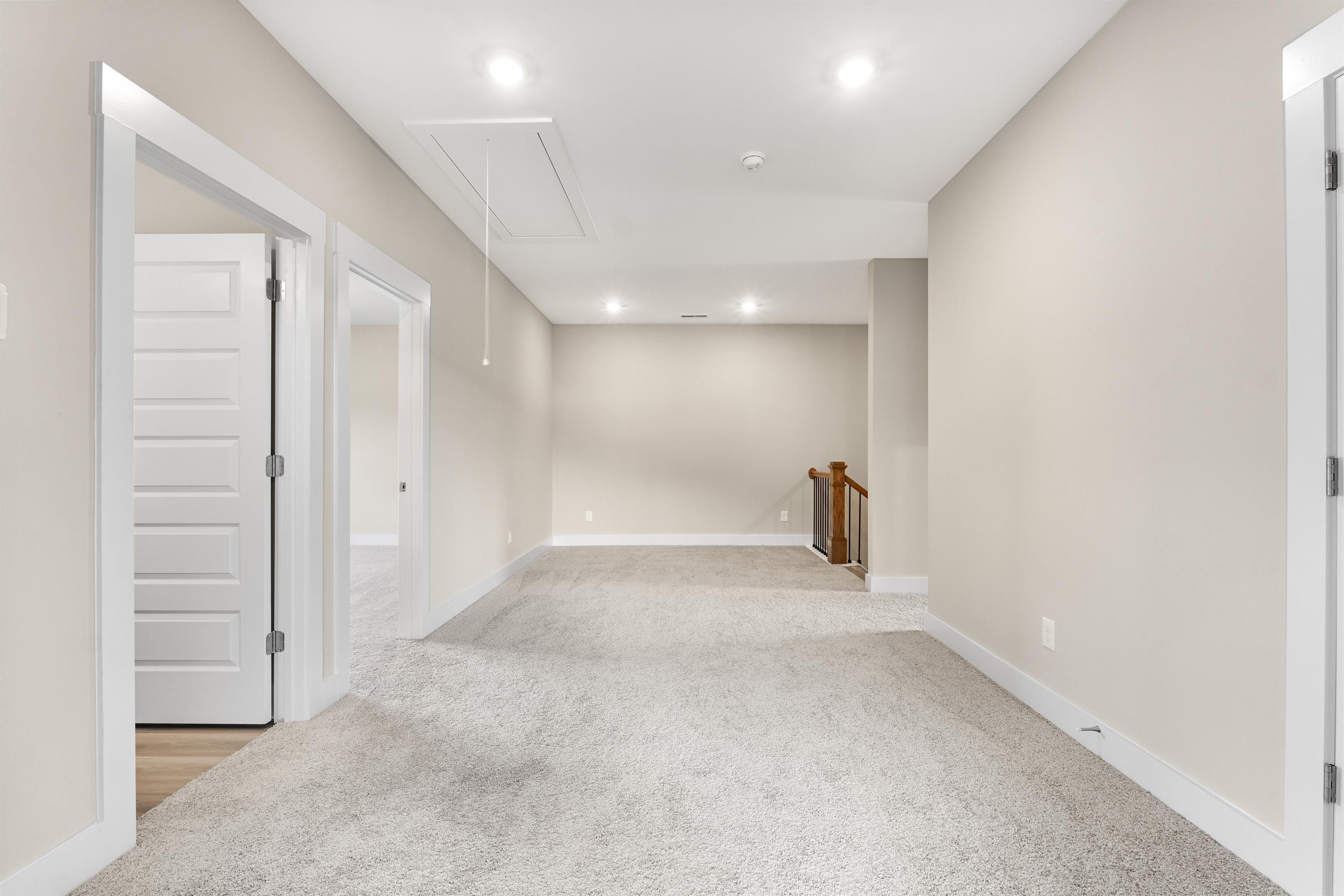 Spacious upstairs hallway in The Oxford A with beige walls, carpeted floors, open doorways, and wooden staircase railing