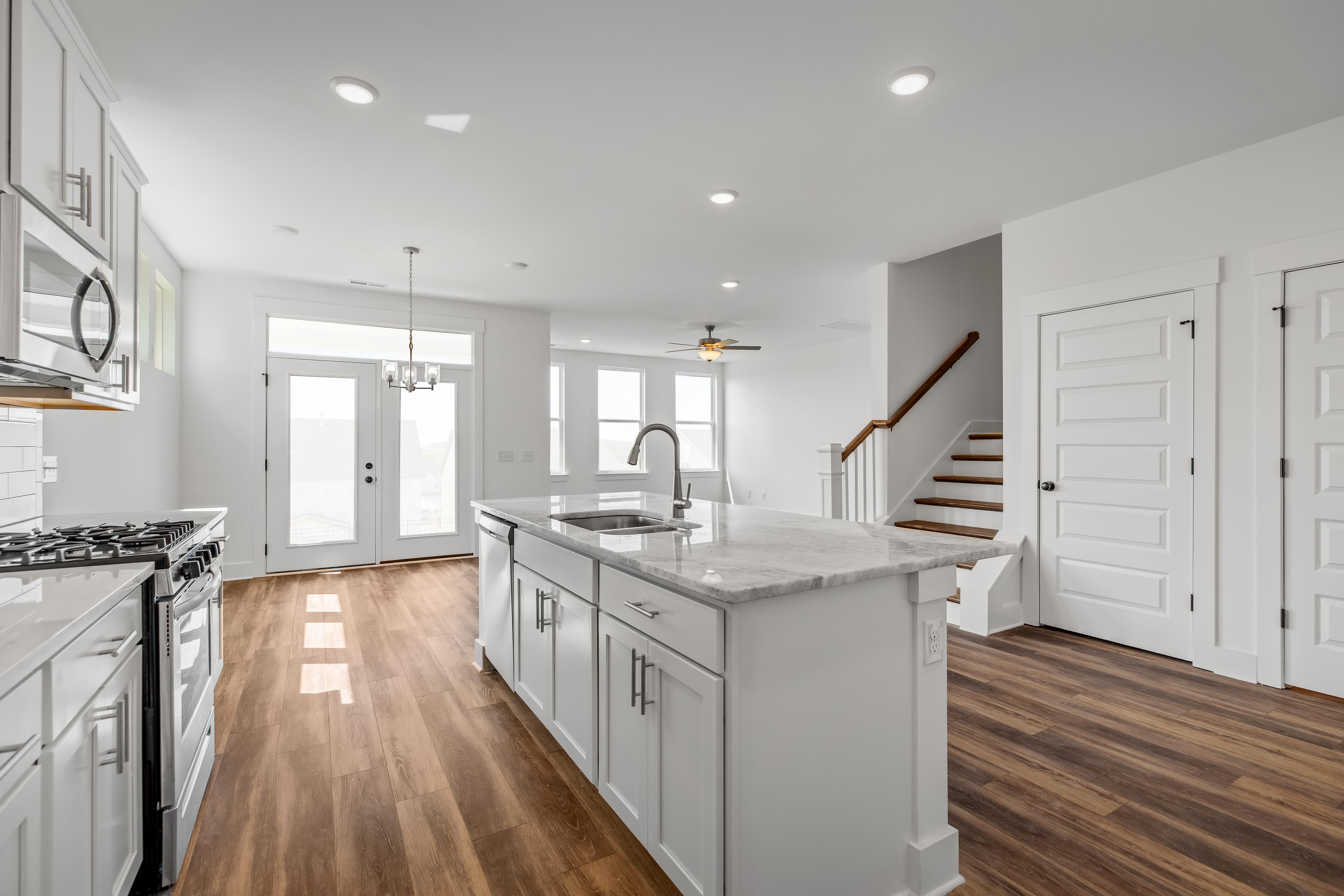 Open-concept kitchen in The Cedar D featuring a large center island, white cabinetry, and wood flooring.