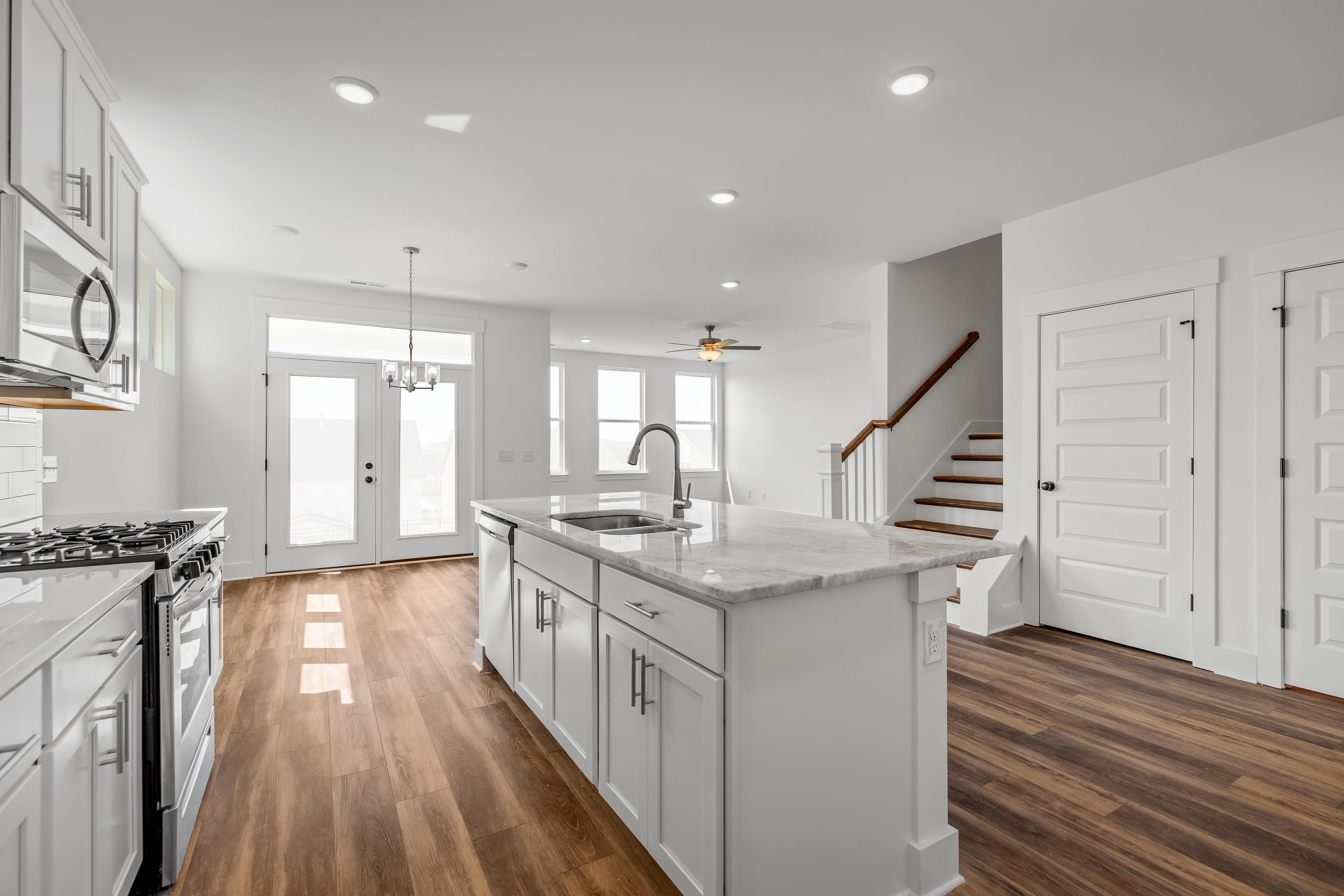 Open-concept kitchen in The Cedar D featuring a large center island, white cabinetry, and wood flooring.