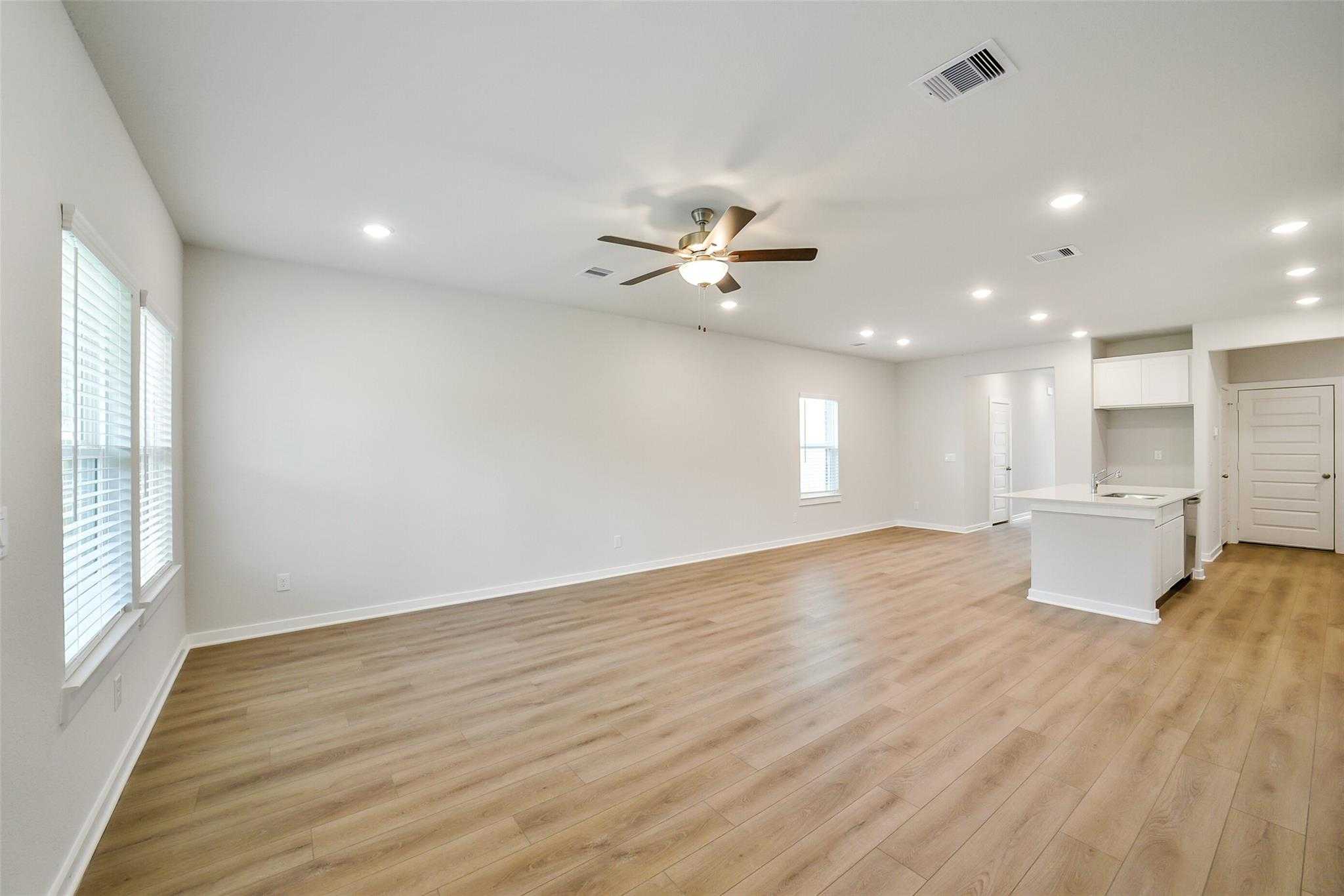 Bright open-concept living room with ceiling fan, luxury vinyl plank floors, and white kitchen island in Davidson Homes The Blanco E, Magnolia, Texas