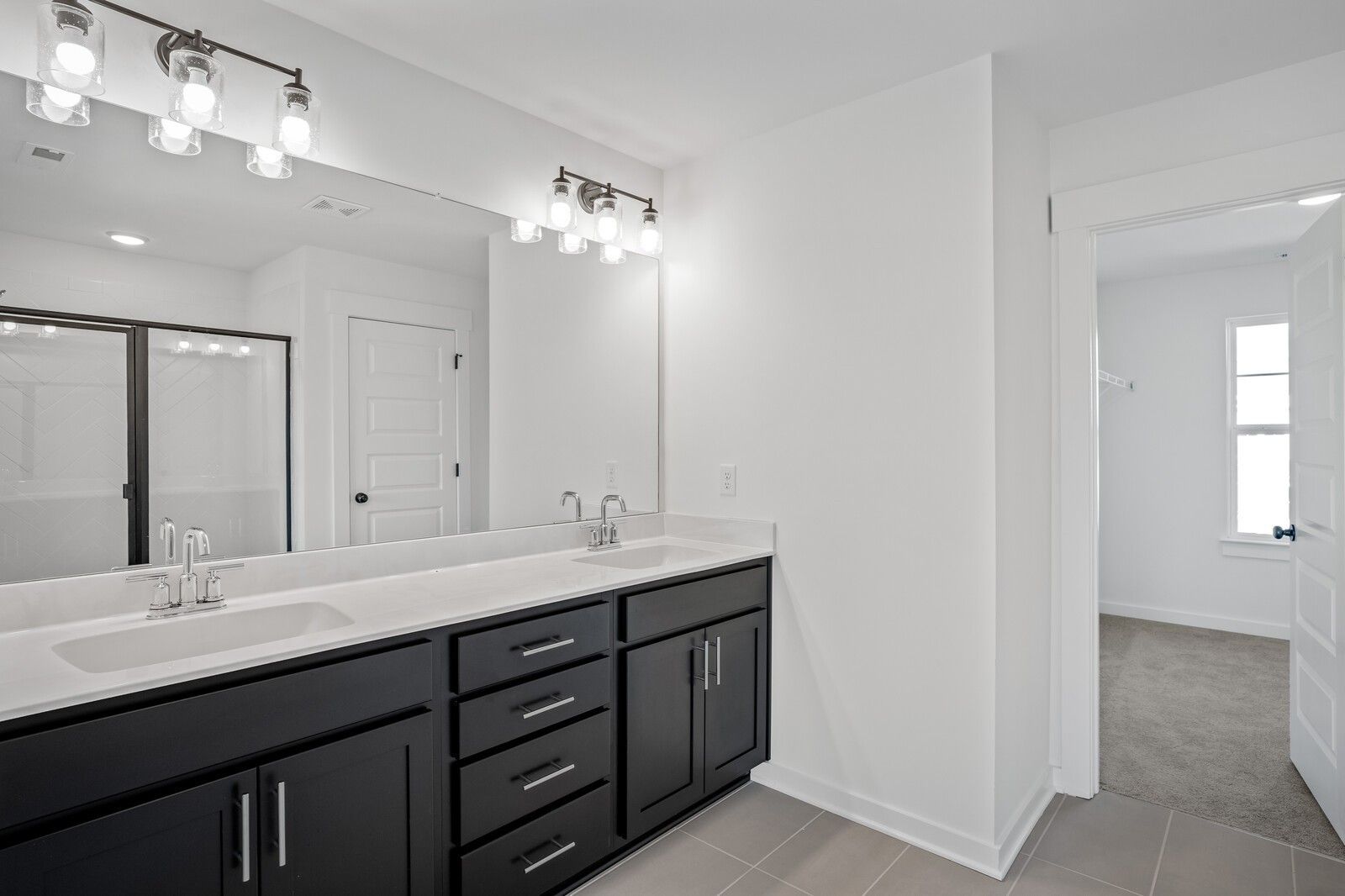 Modern master bathroom featuring double vanity with dark cabinets, white quartz tops, and glass shower in Davidson Homes The Willow C, Gallatin, TN