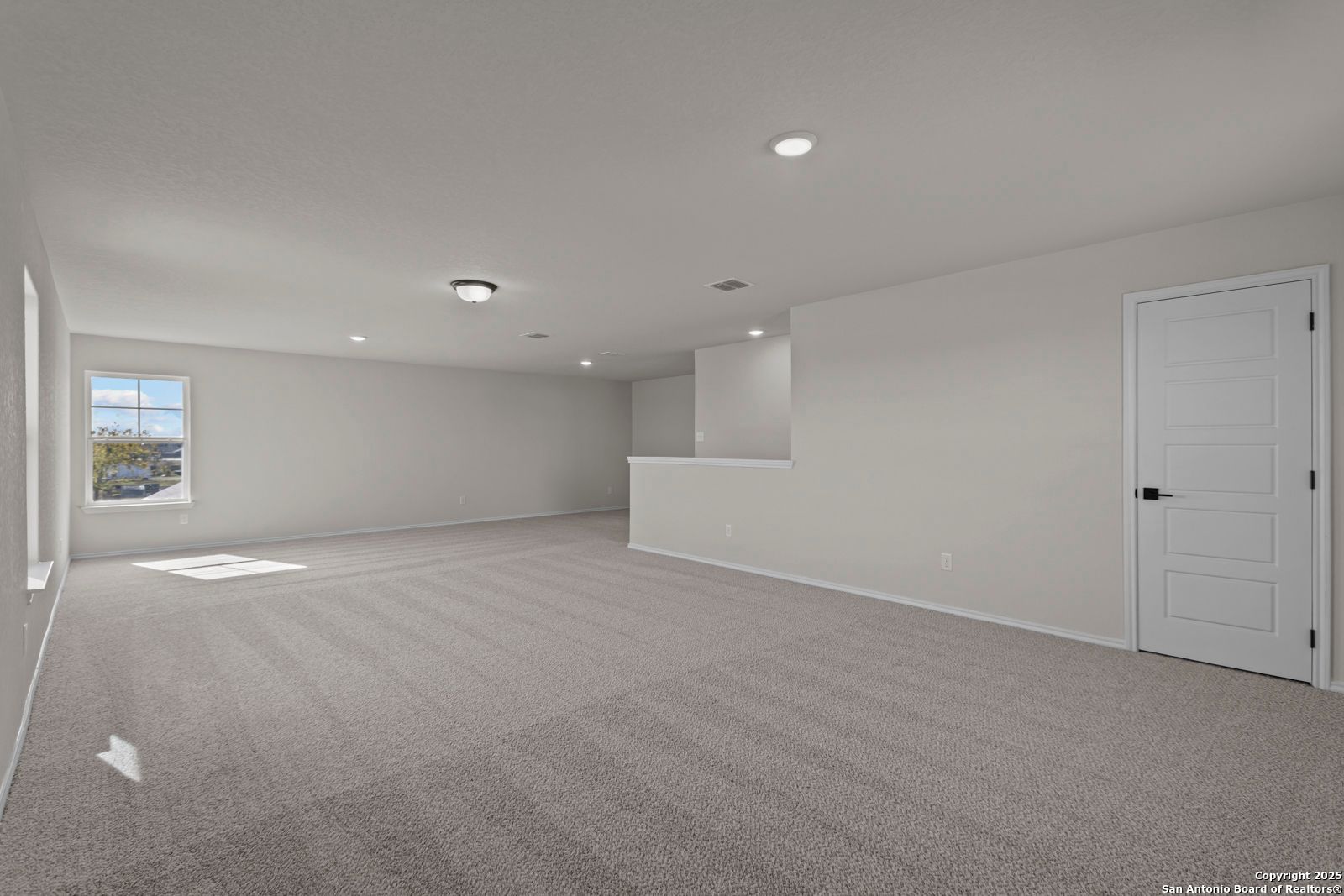 Spacious upstairs loft with gray carpet, large window, and overlook railing in Davidson Homes The Douglas C, Seguin, Texas