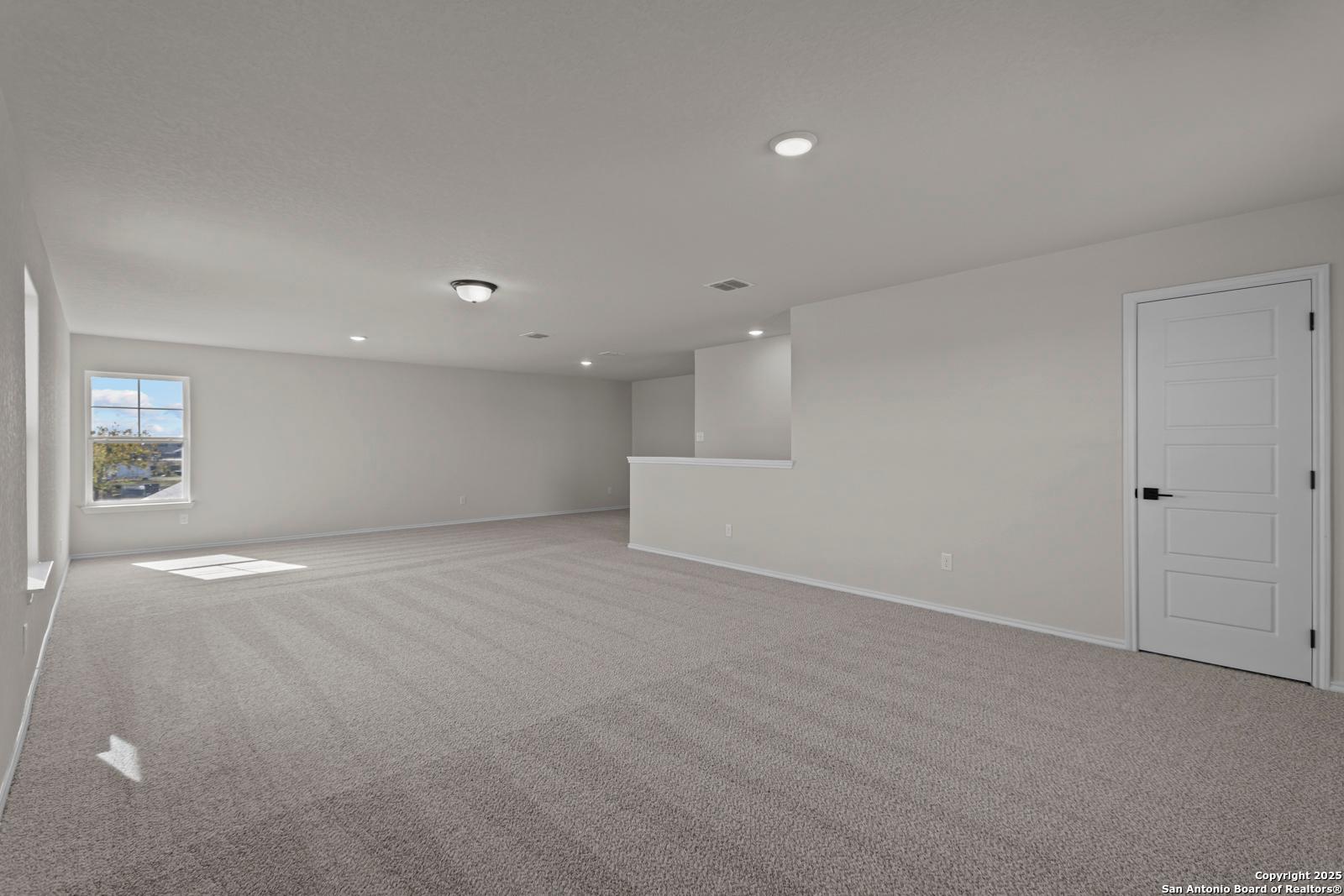 Spacious upstairs loft with gray carpet, large window, and overlook railing in Davidson Homes The Douglas C, Seguin, Texas