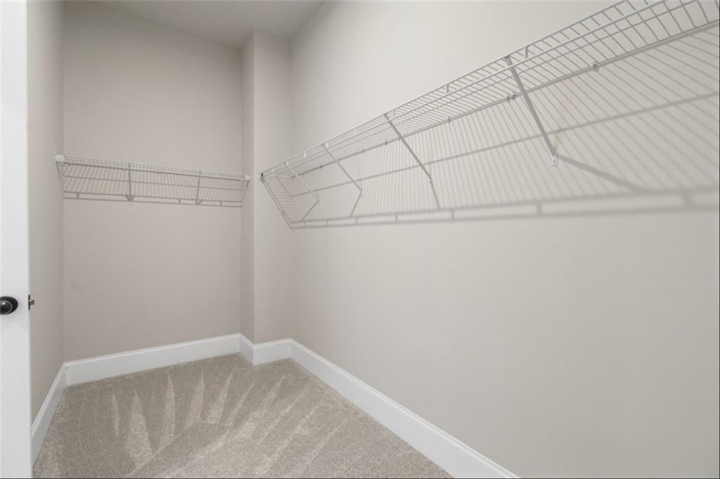 Spacious walk-in closet with wire shelving, beige walls, and carpeted floor in Davidson Homes The Seaside A, Woodstock, GA