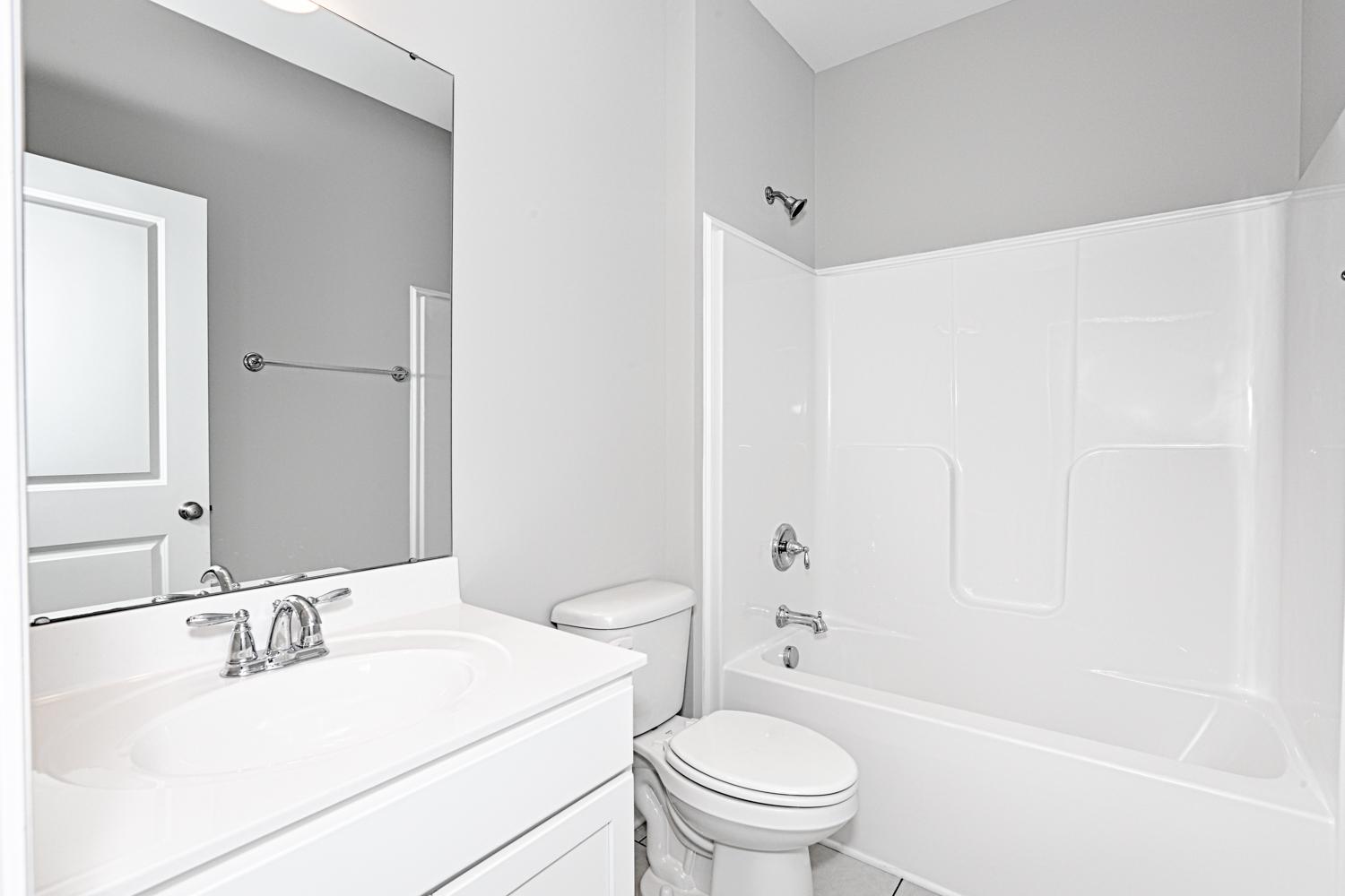 Spacious master bathroom in The Montgomery home with white vanity, large mirror, toilet, and bathtub-shower combo