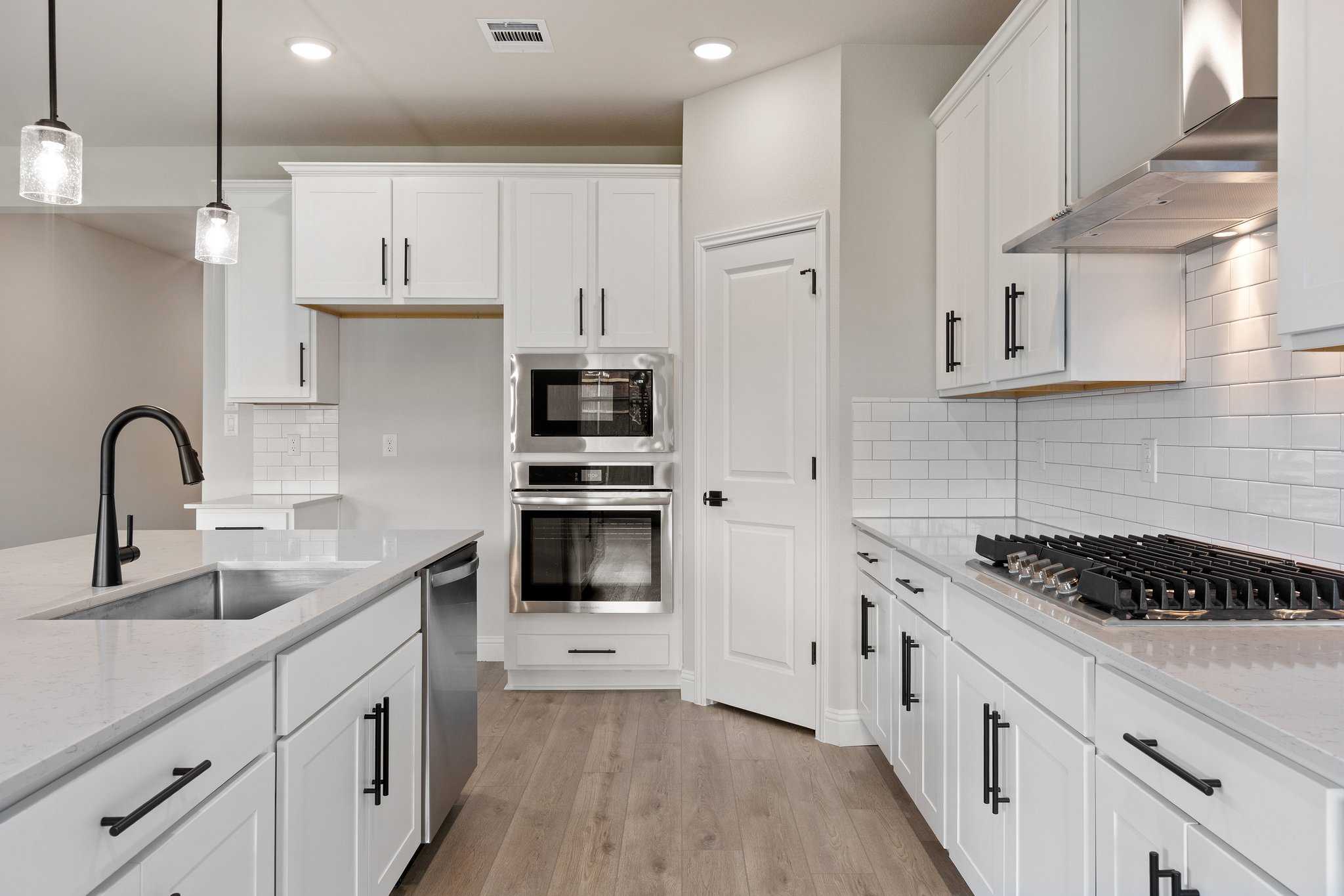 Modern white kitchen in The Harrison C with quartz island, double wall ovens, gas range, subway tile backsplash