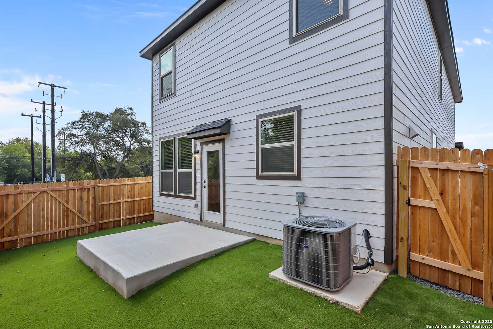 Backyard view of The Florence C two-story home with covered concrete patio, green lawn, wooden fence, and AC unit in Cedar Heights, San Antonio