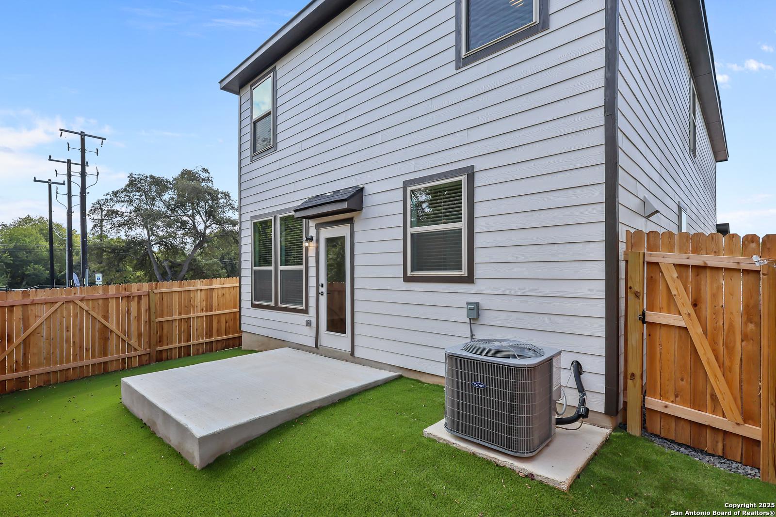 Backyard view of The Florence C two-story home with covered concrete patio, green lawn, wooden fence, and AC unit in Cedar Heights, San Antonio