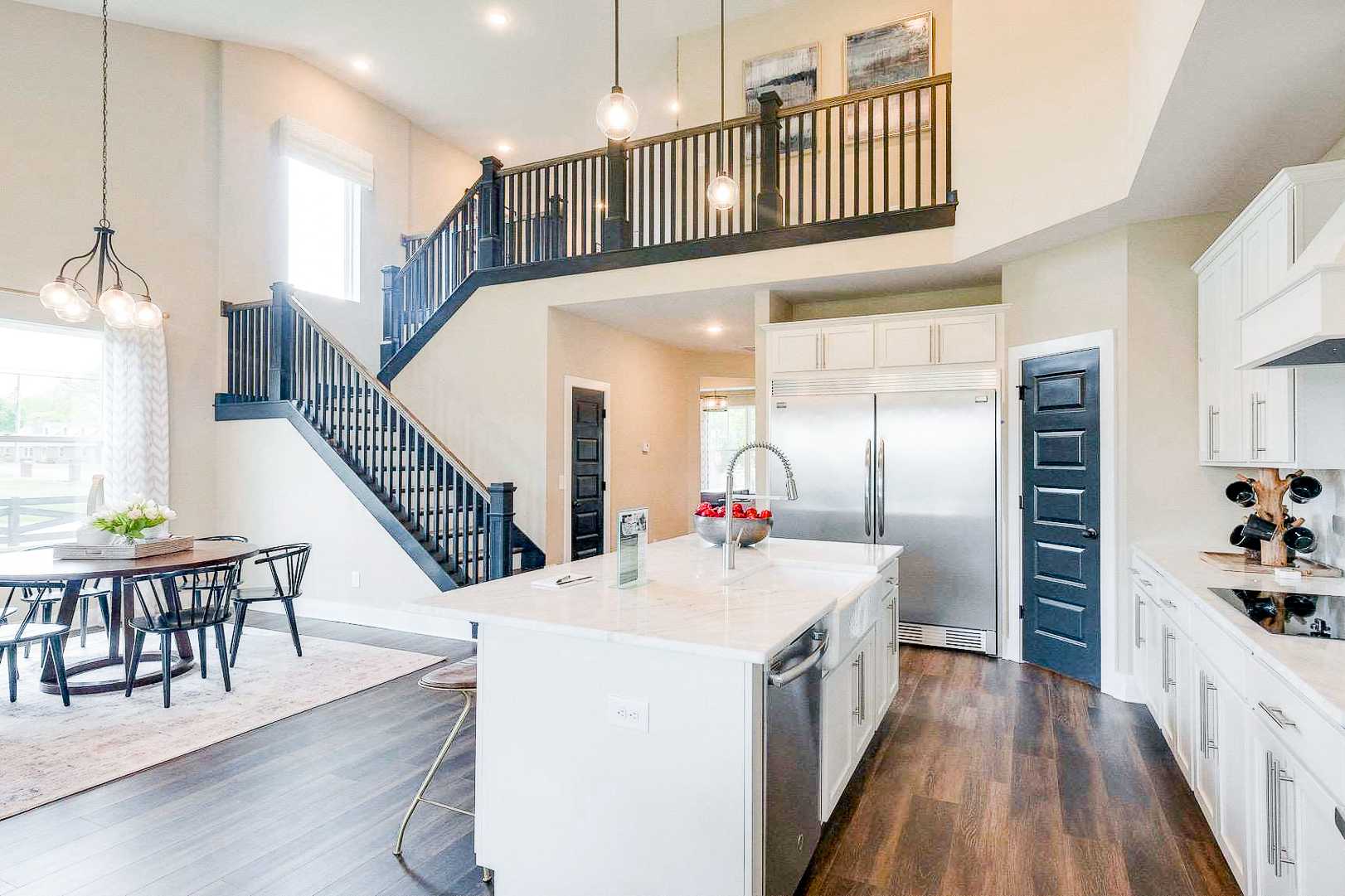 Modern open-concept kitchen with white island, stainless appliances, dining nook, and loft staircase at The Meadows in Smyrna, Tennessee