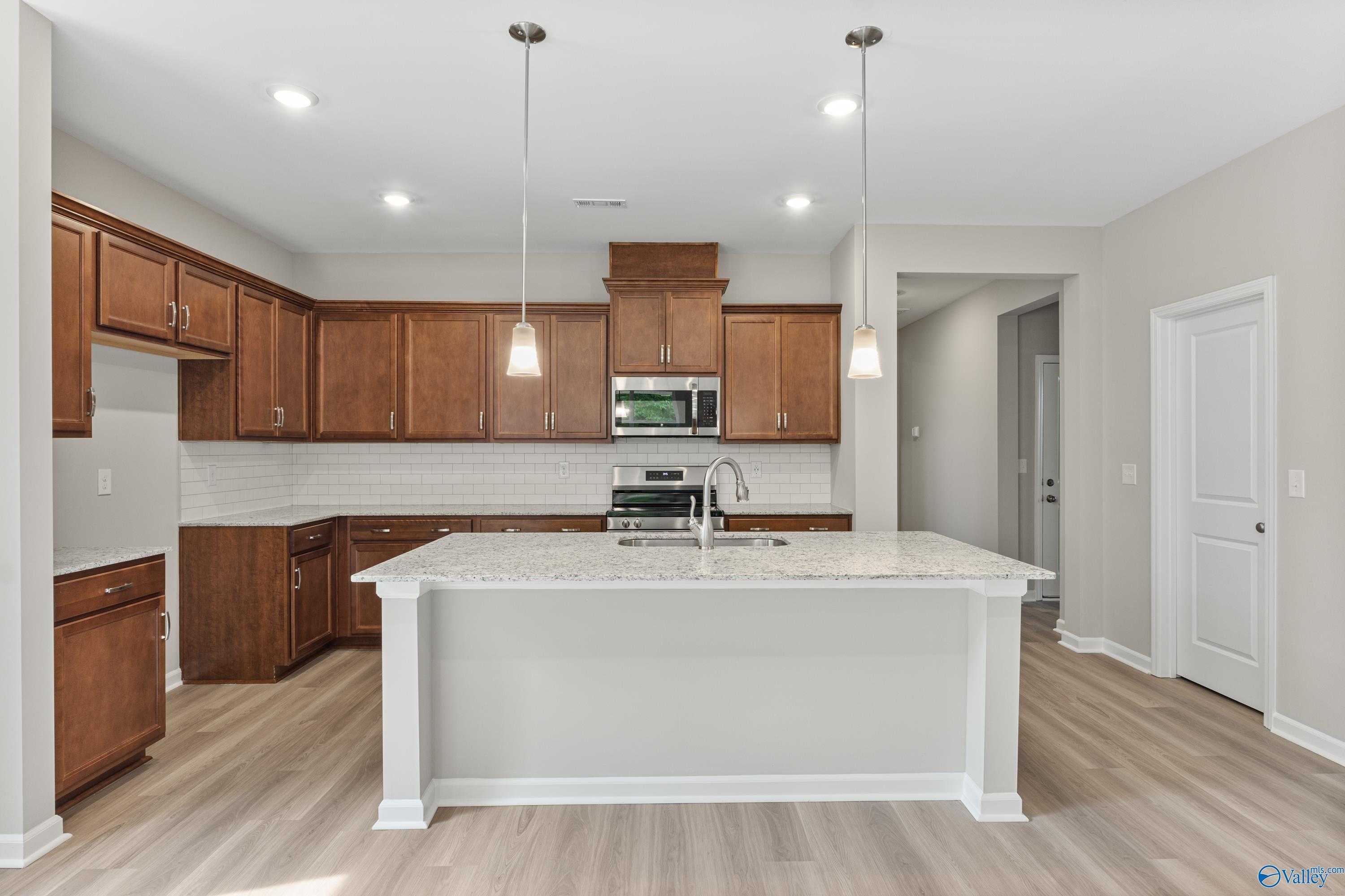 Open-concept kitchen with oak shaker cabinets, subway tile backsplash, stainless appliances, and quartz island in Davidson Homes The Aurora, Fayetteville TN