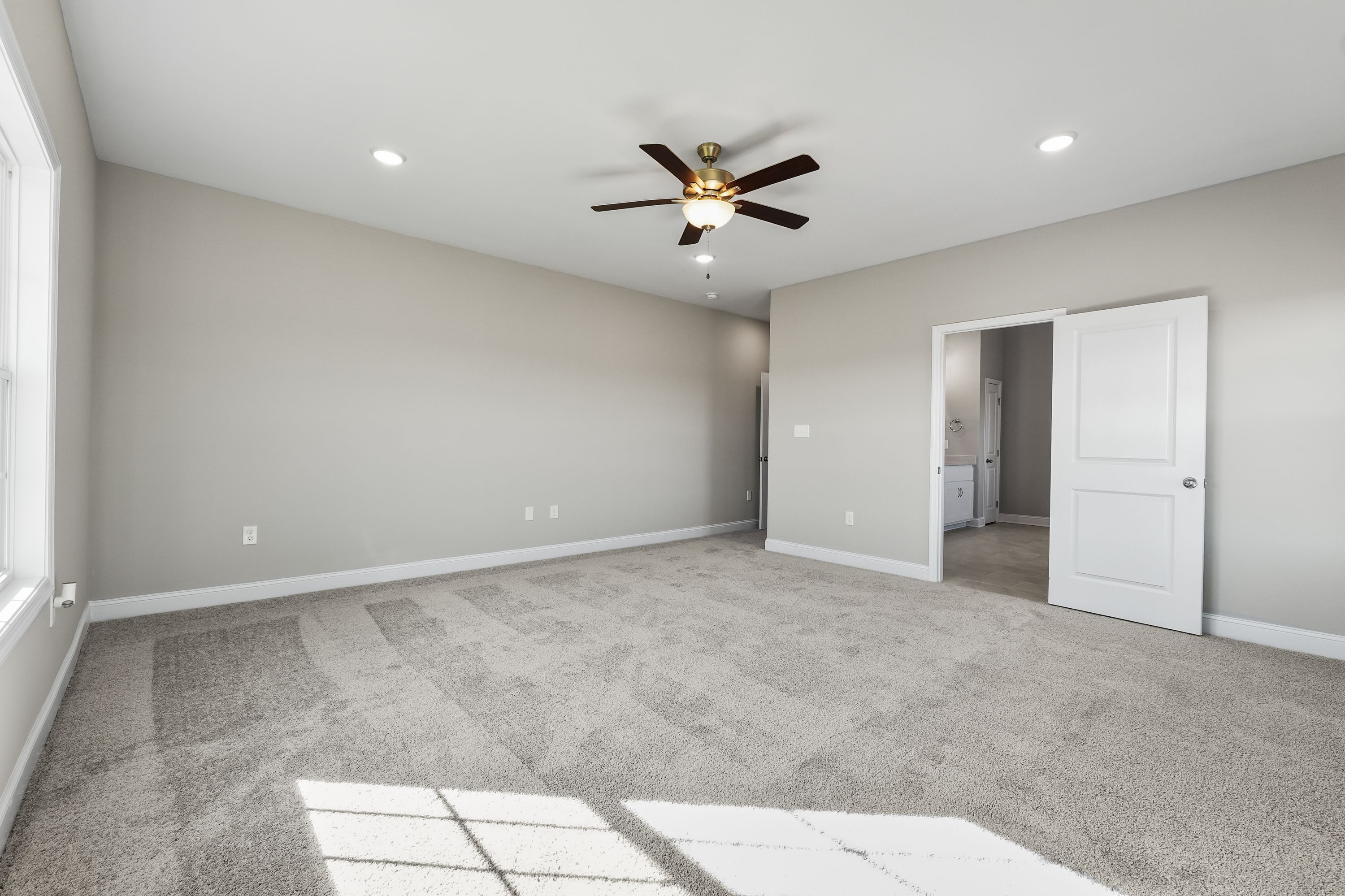 Spacious master bedroom in The Valencia home design with neutral walls, ceiling fan, and adjacent bathroom entry