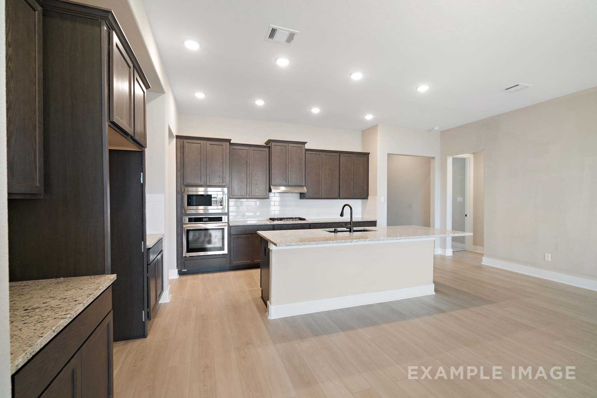 Spacious gourmet kitchen in The Elizabeth A with dark shaker cabinets, large granite island, double ovens, and open layout