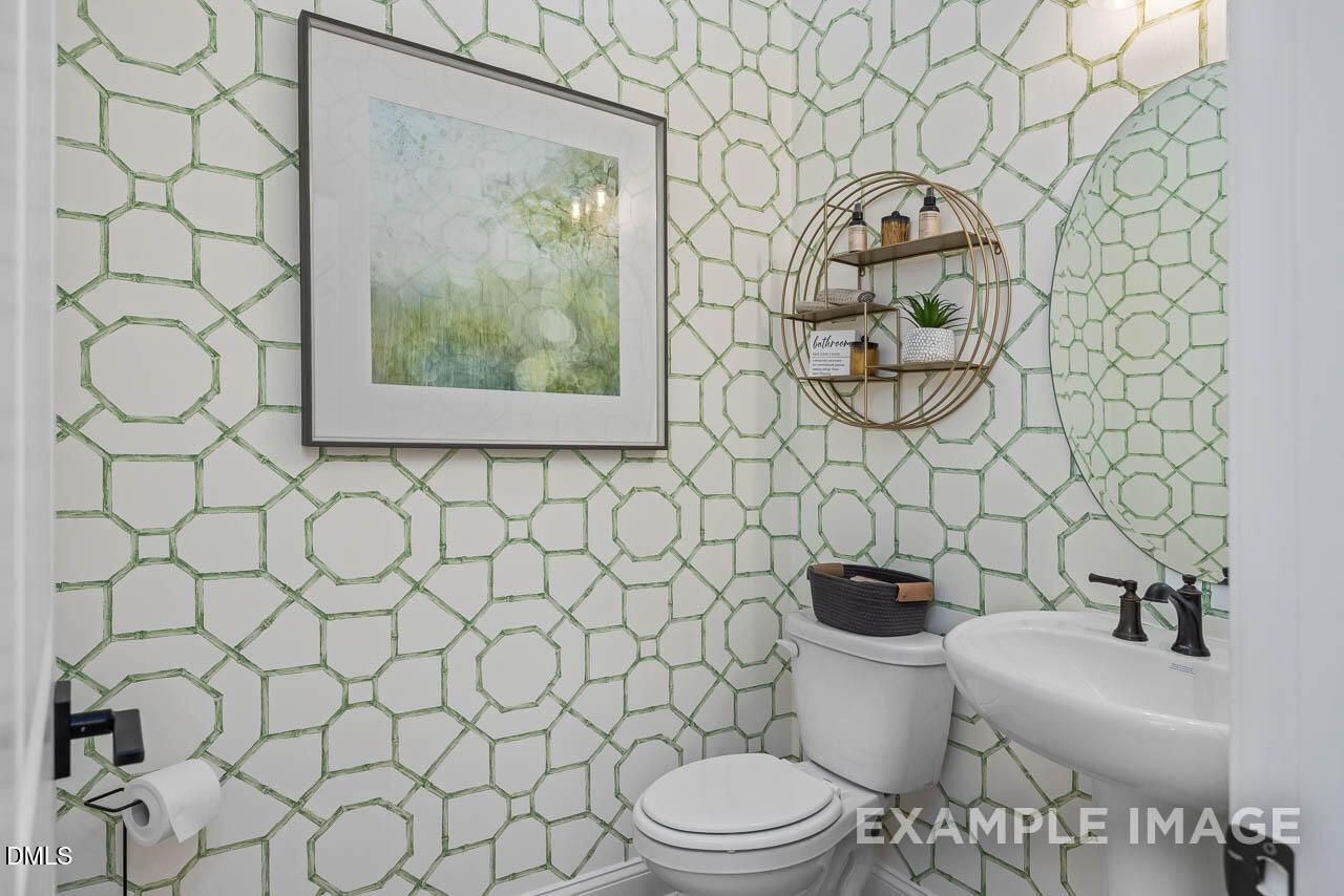 Elegant powder room with green geometric wallpaper, gold round mirror, artwork, sink, and toilet in Davidson Homes The Crawford D, Angier, NC