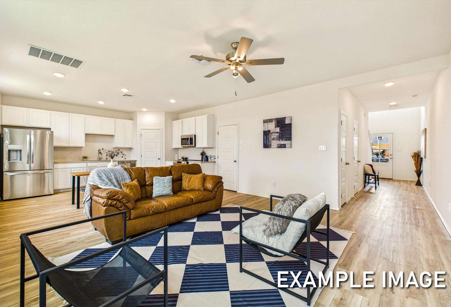 Spacious open-concept living room and kitchen in The Trinity by Davidson Homes, San Antonio, featuring white cabinetry, stainless steel appliances, beige sofa, and checkered rug