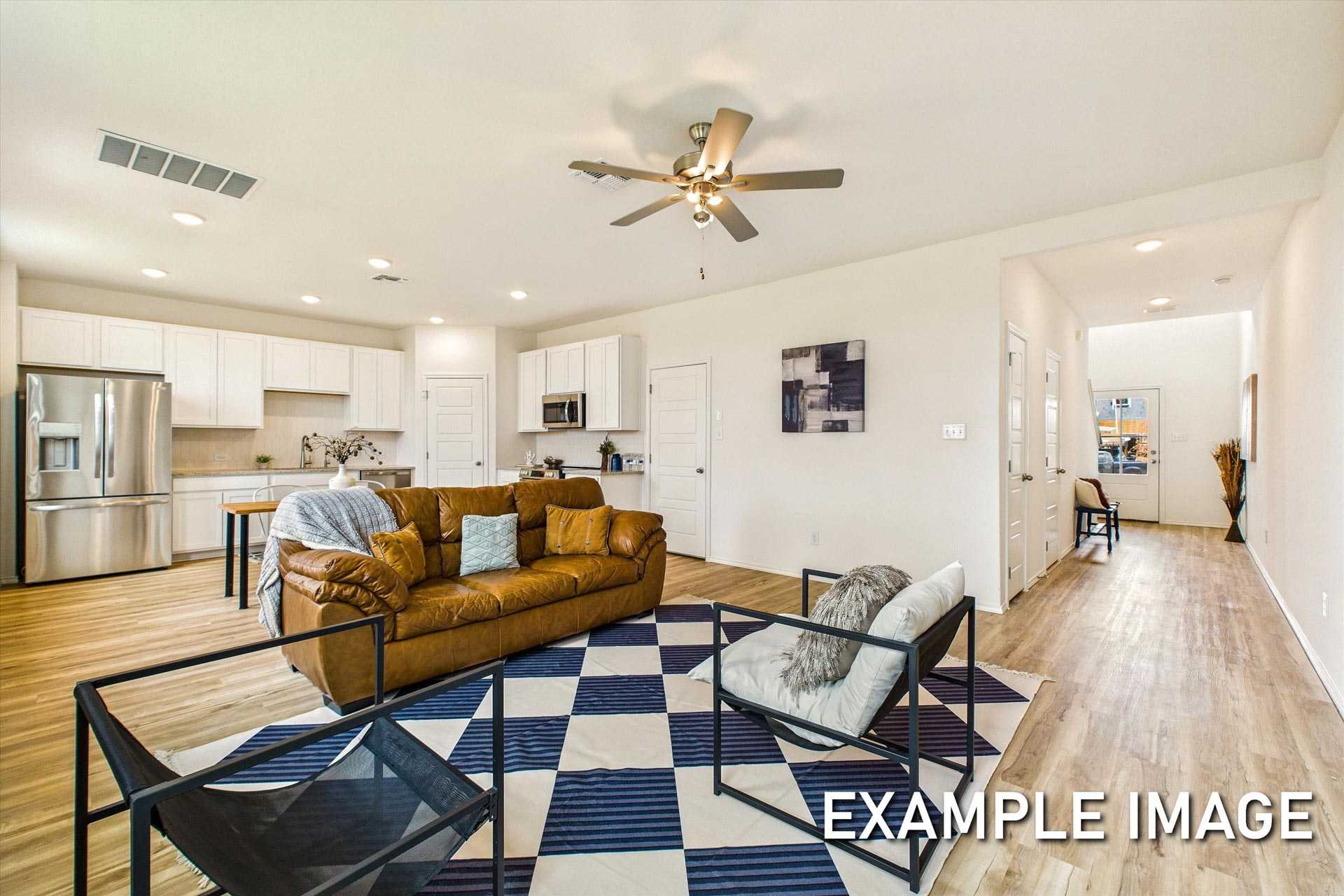 Open-concept living room in The Trinity B by Davidson Homes, with leather sofa on checkered rug, white kitchen, and ceiling fan