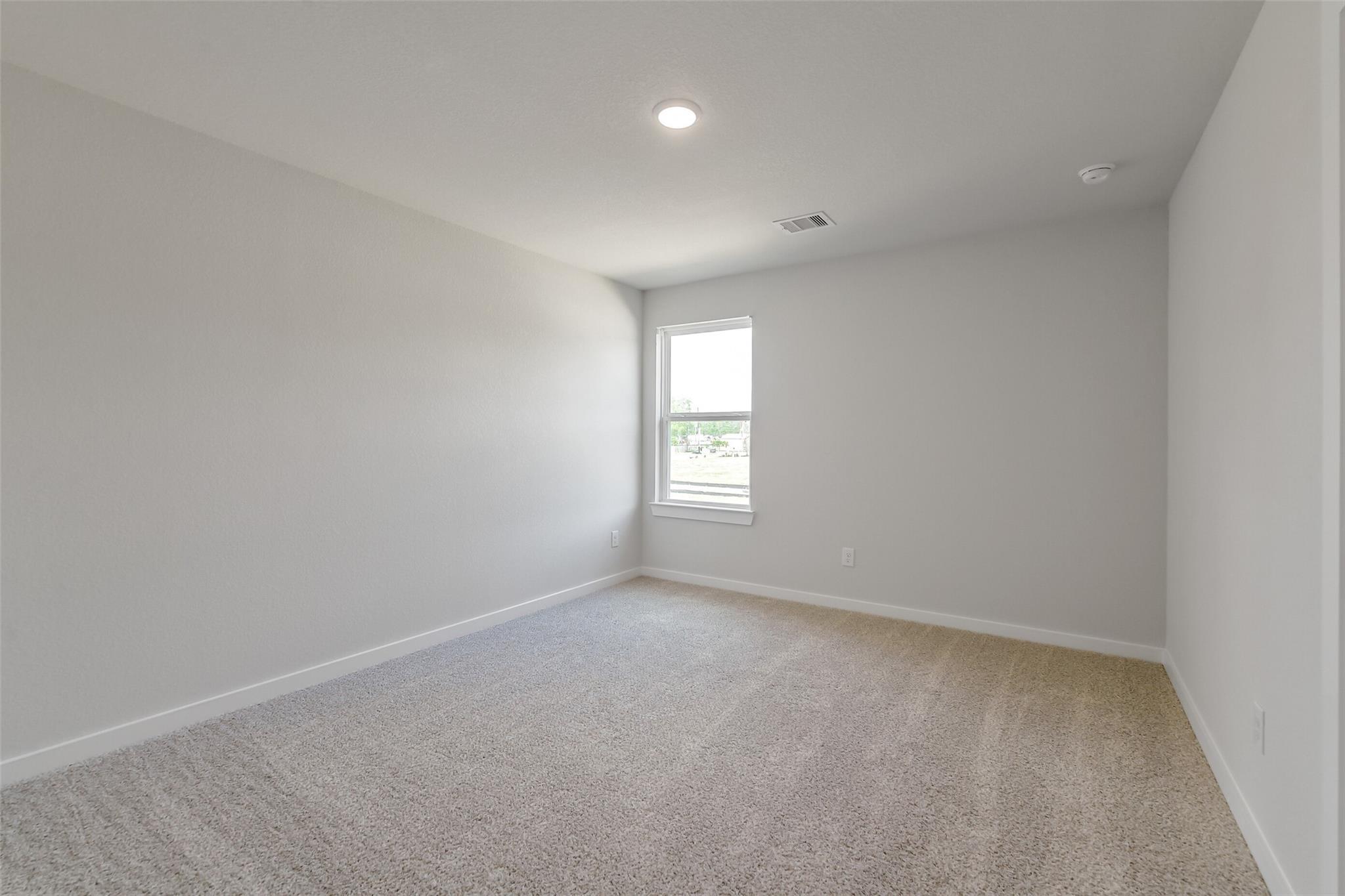 Bright secondary bedroom with light gray walls, beige carpet, and sunny window in Davidson Homes San Marcos E, Conroe Texas