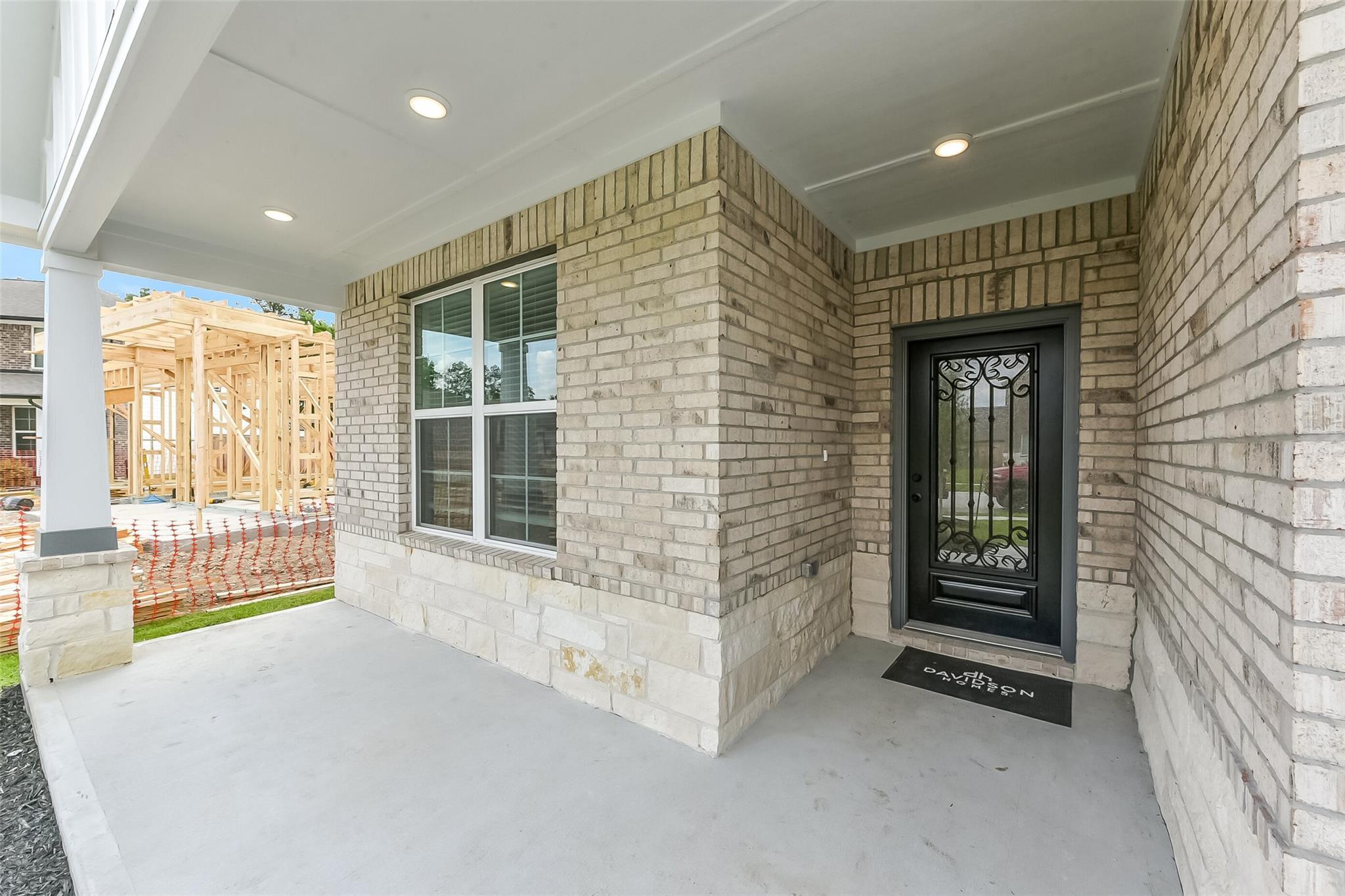 Elegant brick front entrance with black wrought iron door, large windows, and covered porch in Davidson Homes The Everett C, Sundance Cove, Crosby Texas