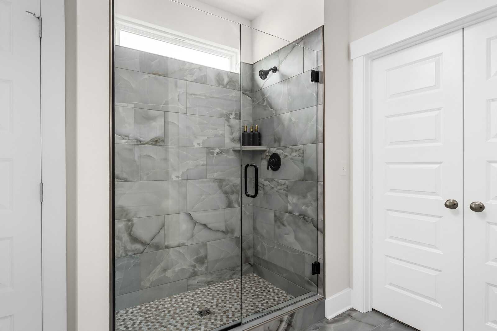 Spacious walk-in shower at Woods Crossing in Gallatin Tennessee with gray subway tile, glass enclosure, and pebble floor by Davidson Homes
