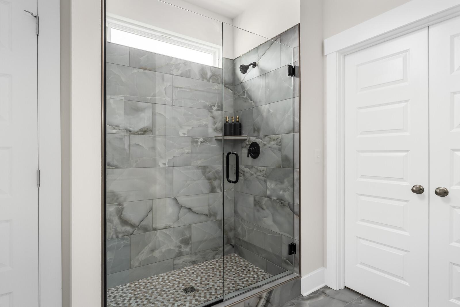 Spacious walk-in shower at Woods Crossing in Gallatin Tennessee with gray subway tile, glass enclosure, and pebble floor by Davidson Homes