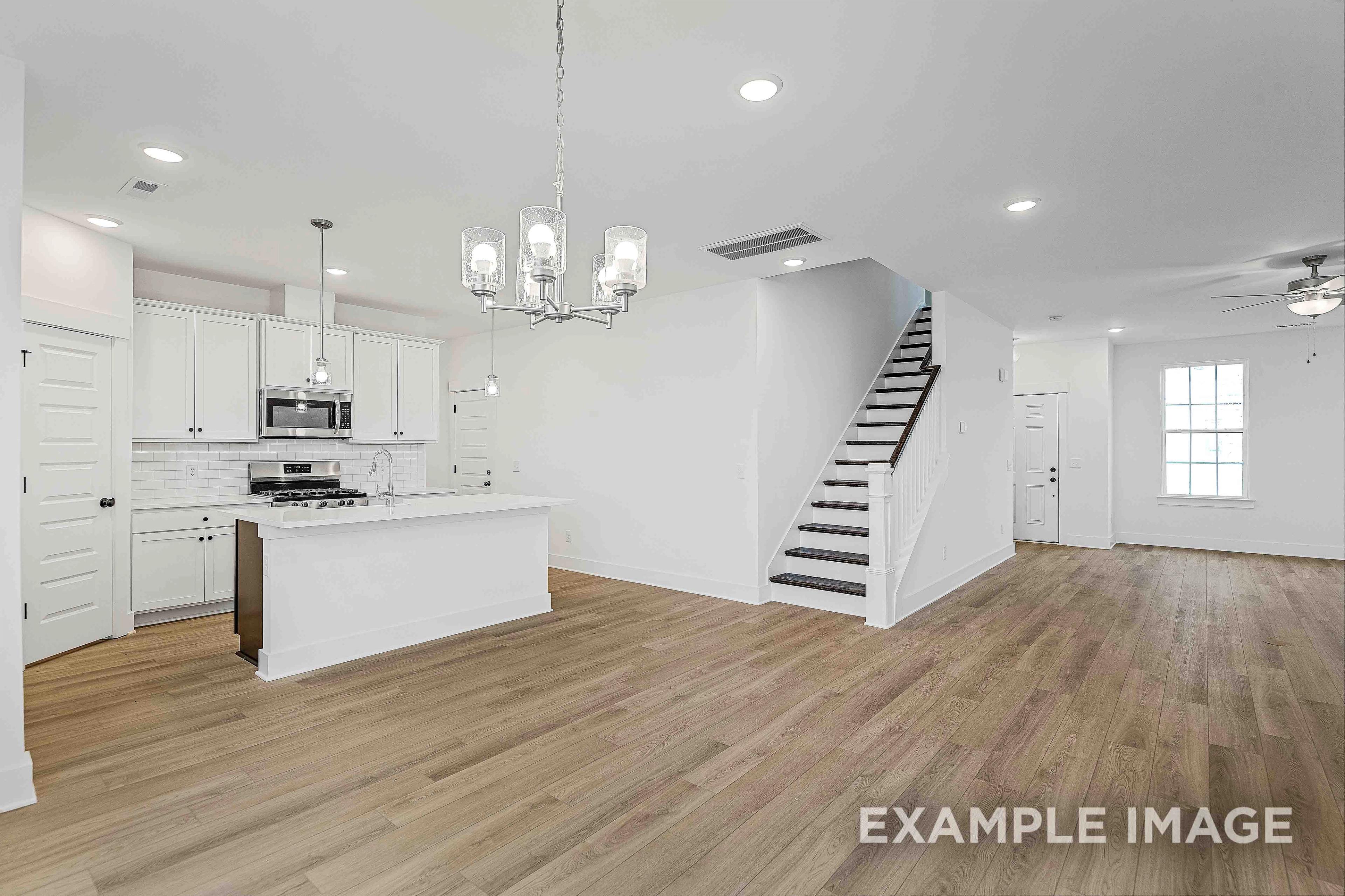 Spacious open-concept kitchen in The Charleston C home featuring white cabinets, stainless appliances, large island, hardwood floors, and staircase