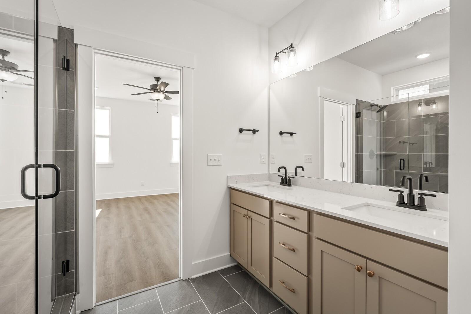 Modern master bathroom featuring double beige vanity, white quartz counters, glass shower, and ceiling fan view in Davidson Homes The Ash A, Gallatin TN