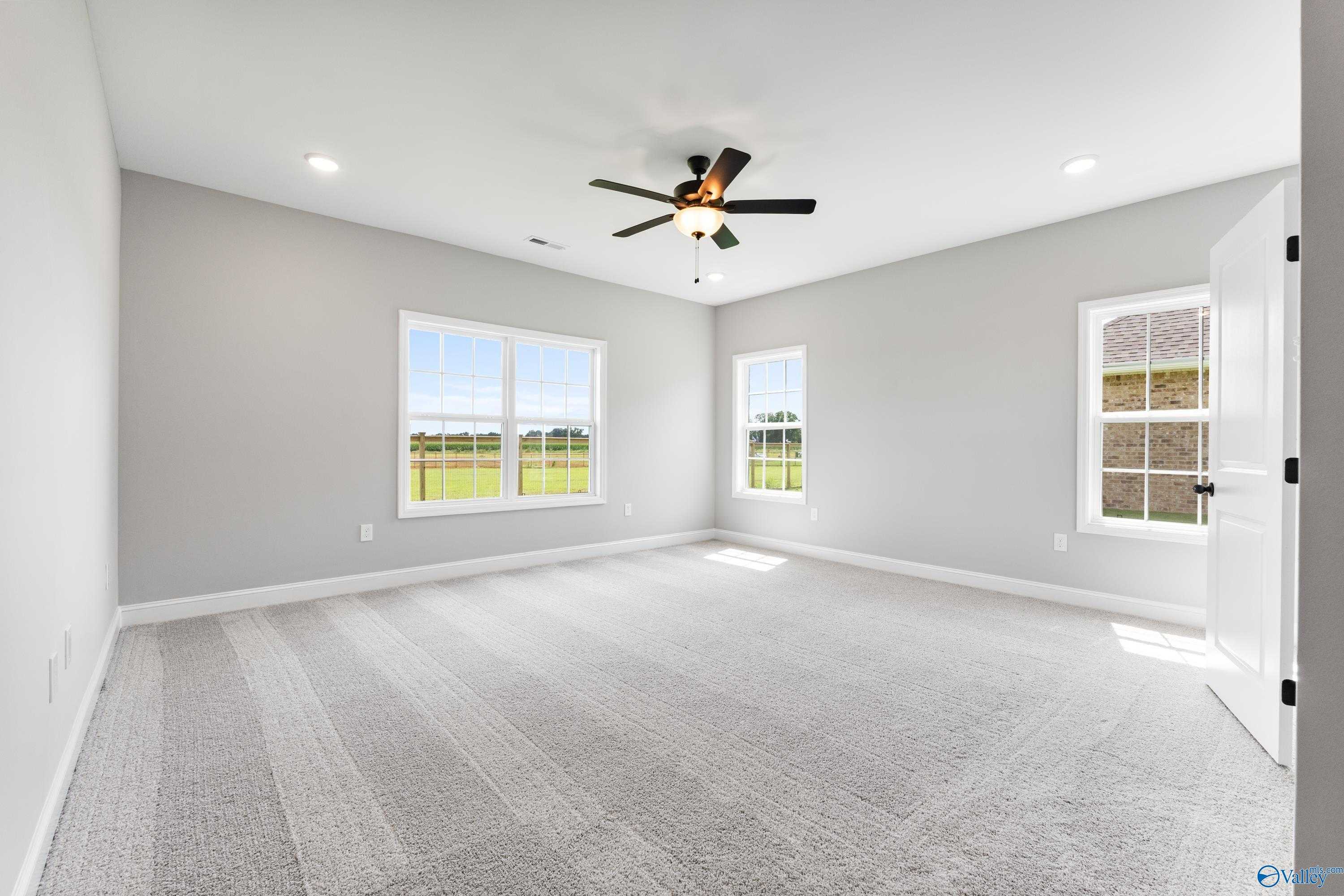 Bright bedroom with large windows overlooking green fields, ceiling fan, and plush gray carpet in Davidson Homes The Finleigh, Toney, Alabama