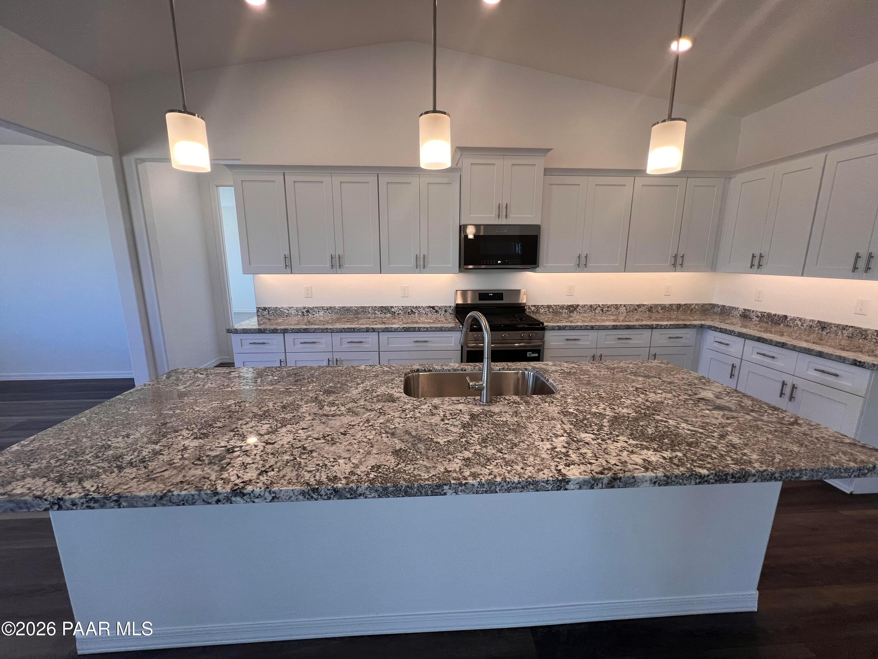 Modern white kitchen with granite island, stainless appliances, and pendant lights in Davidson Homes Sunrise II A, Prescott AZ