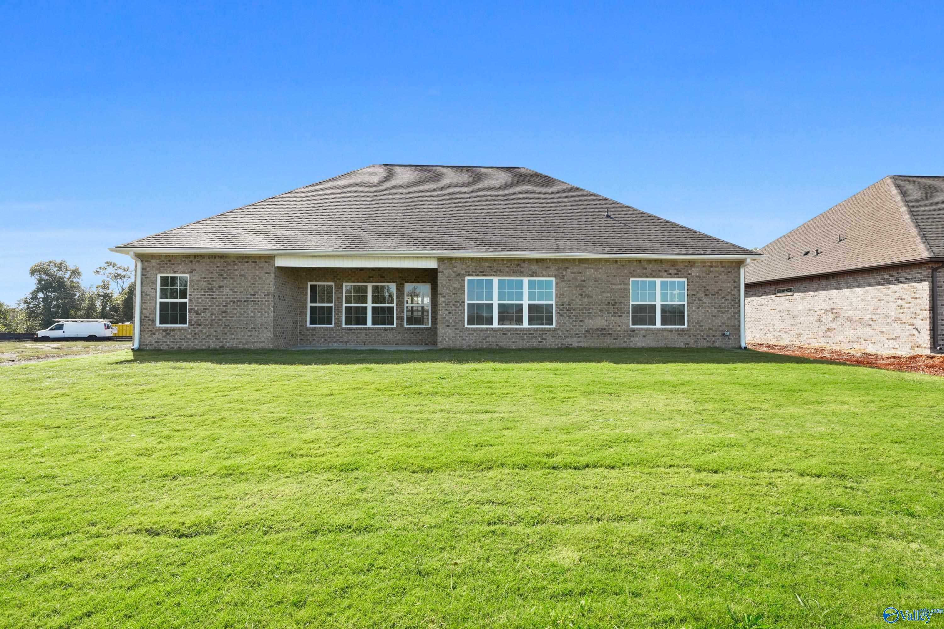 Rear view of single-story brick Finleigh home with large windows, covered patio, and expansive green lawn in Creekside, Harvest, Alabama