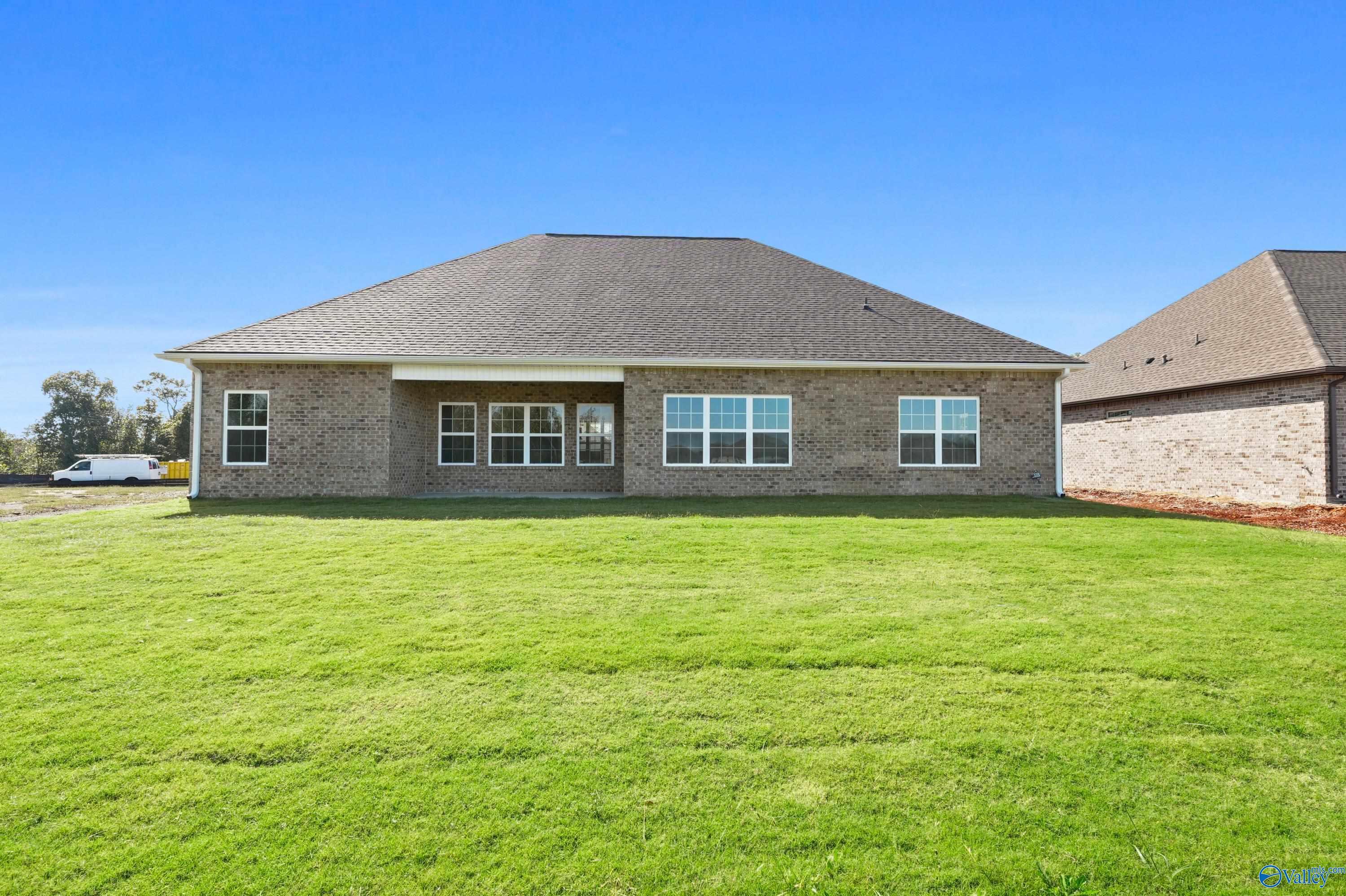 Rear view of single-story brick Finleigh home with large windows, covered patio, and expansive green lawn in Creekside, Harvest, Alabama