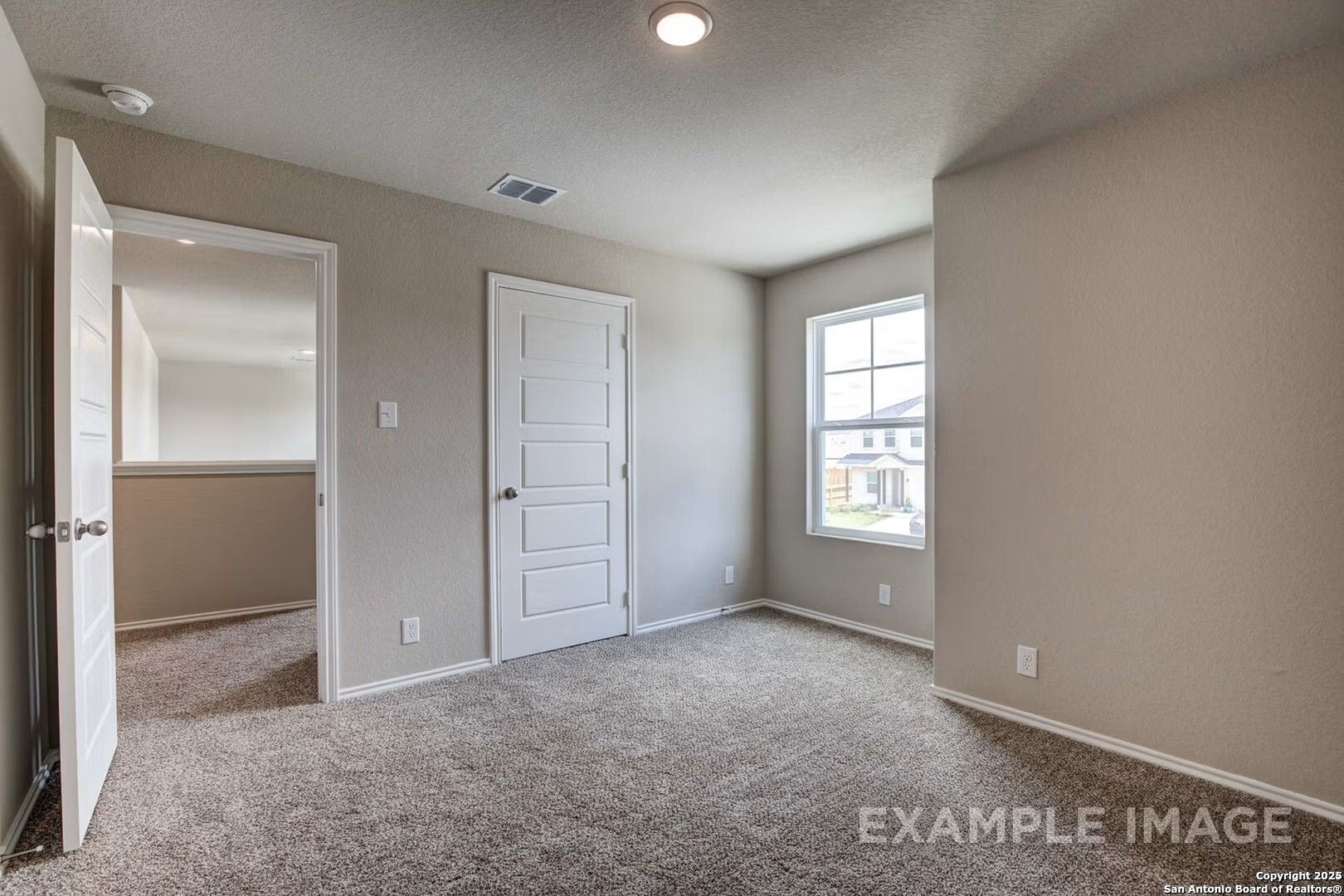Spacious empty bedroom with beige walls, carpet floor, large window, and walk-in access in Davidson Homes The Murray K, San Antonio