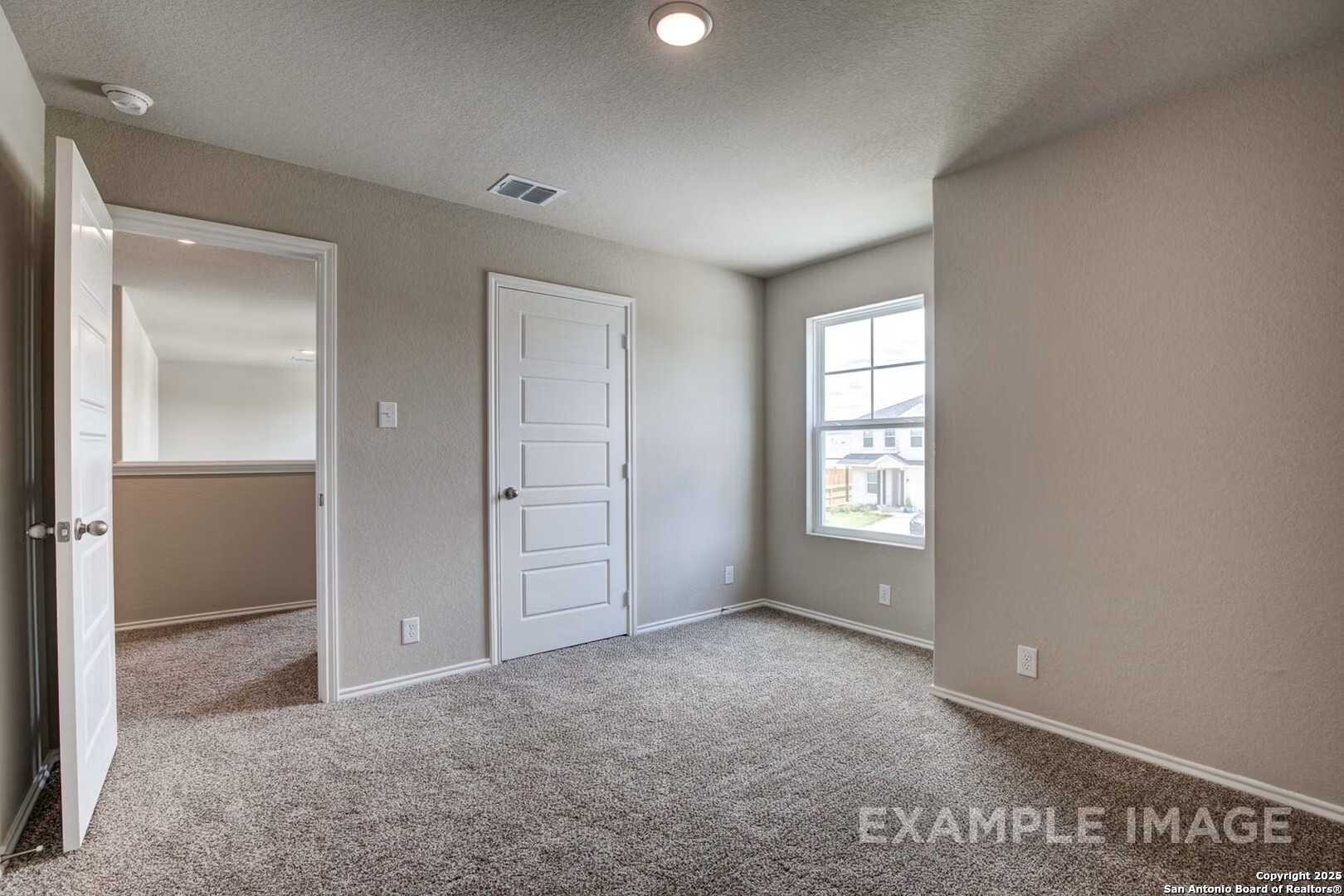 Spacious empty bedroom with beige walls, carpet floor, large window, and walk-in access in Davidson Homes The Murray K, San Antonio