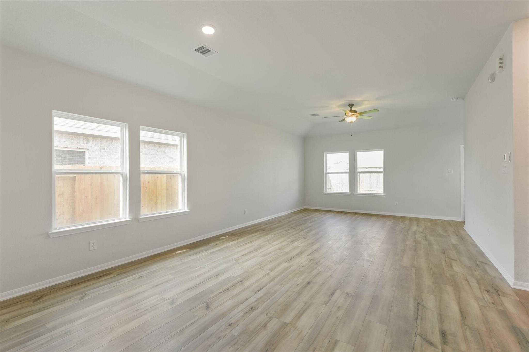 Bright open living room with light wood floors, large windows, ceiling fan in Davidson Homes The Laguna B, Dayton, Texas