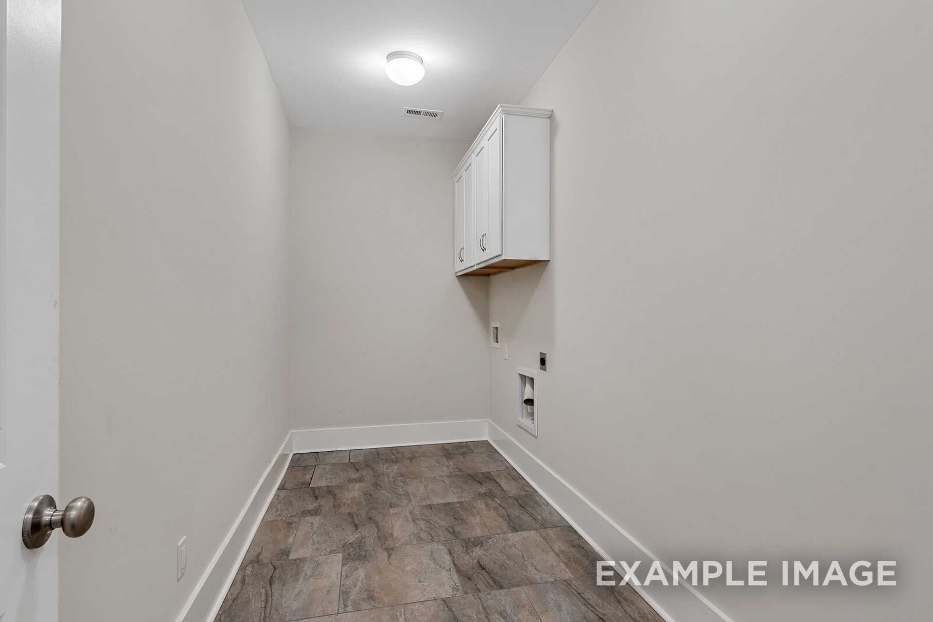 Spacious laundry room in The Rockford home design with white upper cabinet, washer-dryer hookups, beige walls, and wood-look flooring