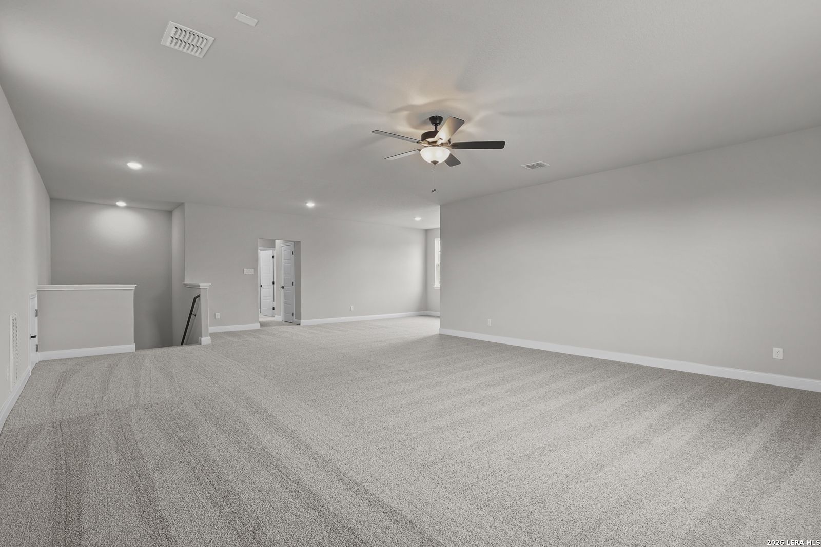 Spacious upstairs loft with gray carpeted floors, neutral walls, ceiling fan, and staircase overlook in Davidson Homes Belmont H, Castroville, Texas