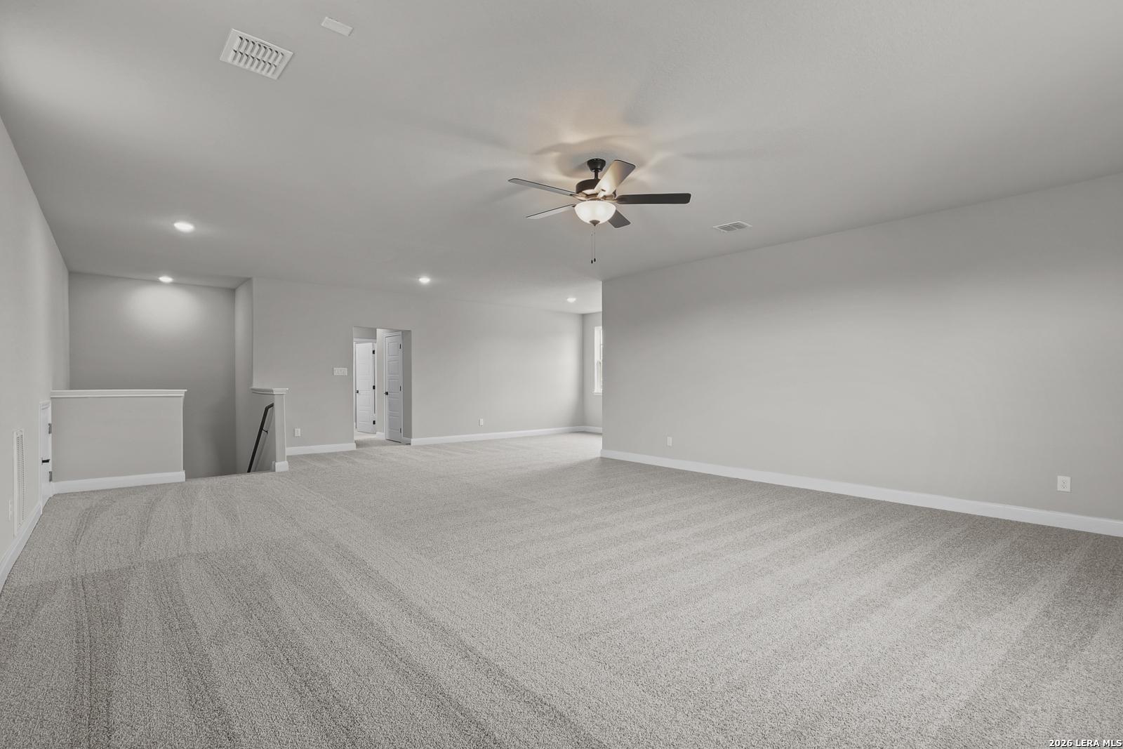 Spacious upstairs loft with gray carpeted floors, neutral walls, ceiling fan, and staircase overlook in Davidson Homes Belmont H, Castroville, Texas