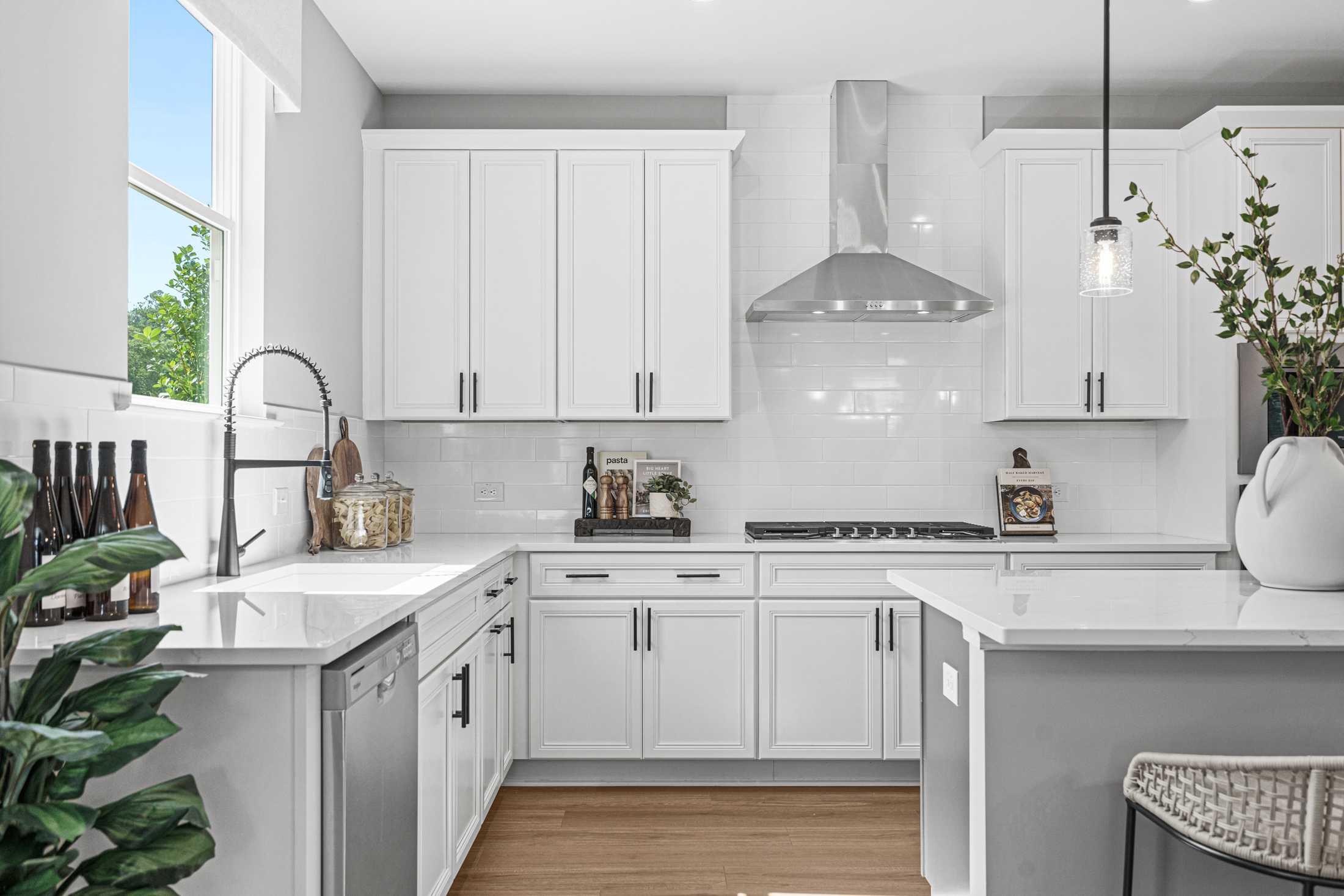 Spacious modern kitchen in The Hickory A featuring white shaker cabinets, stainless steel appliances, gray quartz island, and pendant lights
