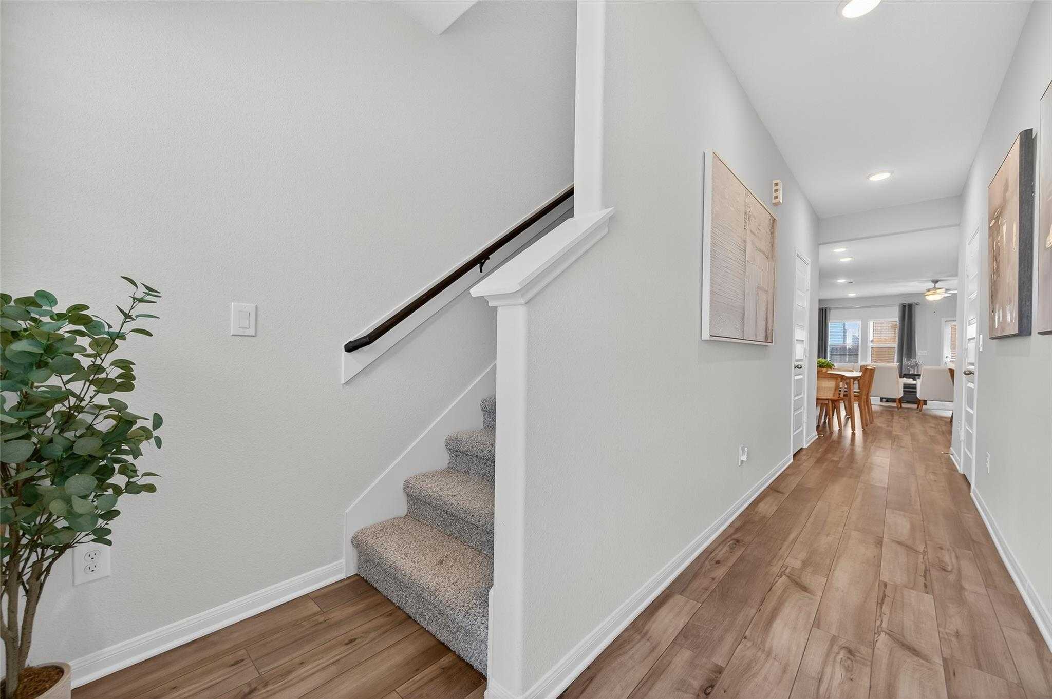 Bright hallway with light wood floors, carpeted staircase, potted plant and dining nook in Davidson Homes The Brazos E, Magnolia, Texas